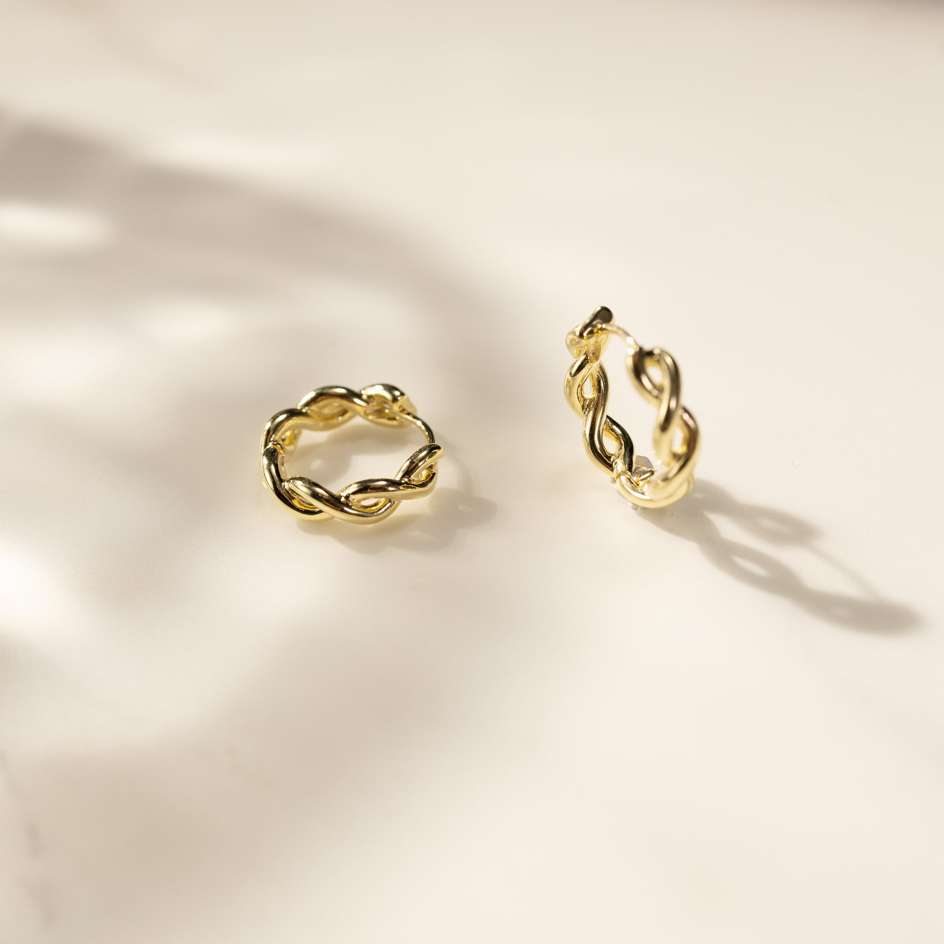 Eva 14K gold vermeil twisted link huggie earrings close-up lifestyle shot on light background, shiny small gold hoops by Silvbreeze.