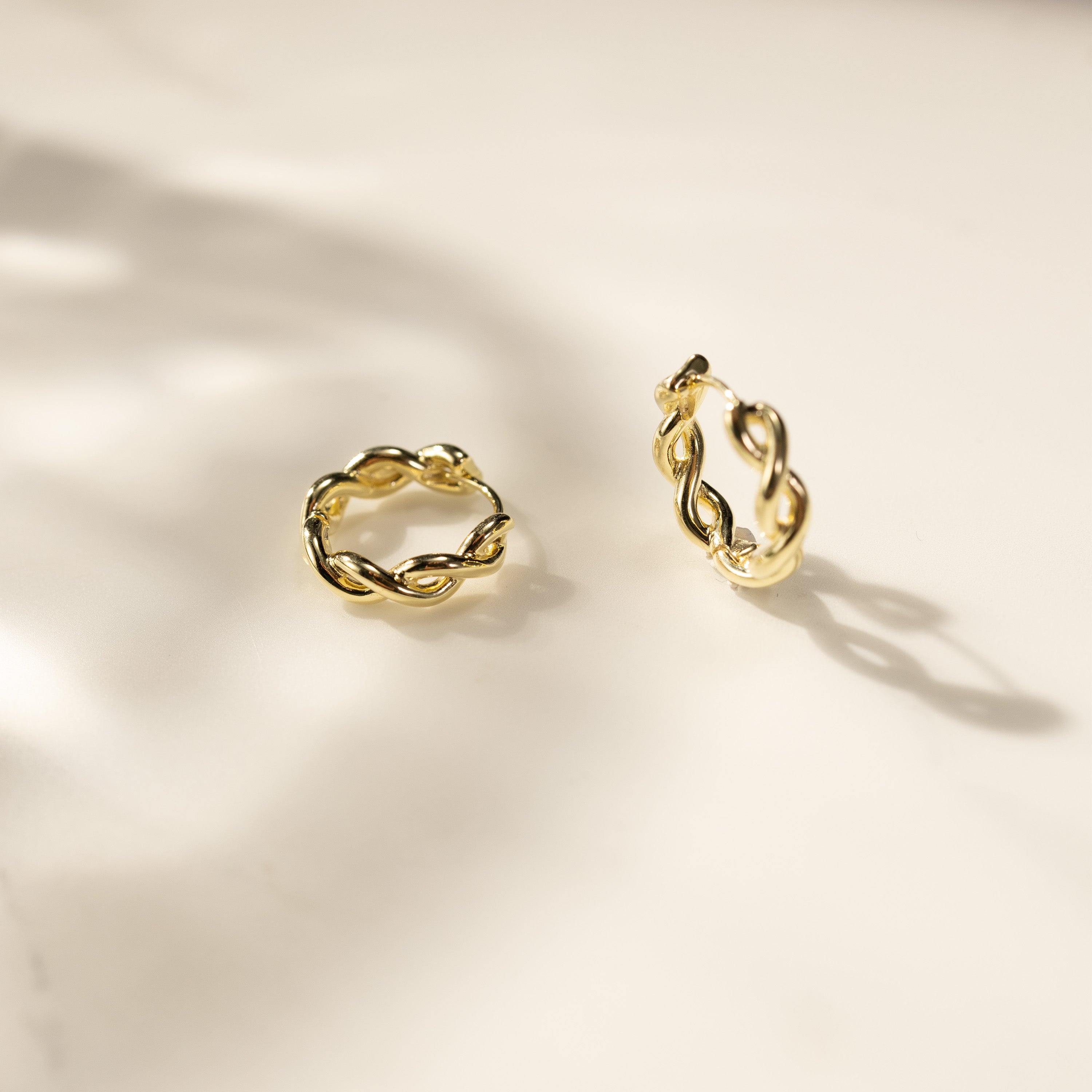 Eva 14K gold vermeil twisted link huggie earrings close-up lifestyle shot on light background, shiny small gold hoops by Silvbreeze.