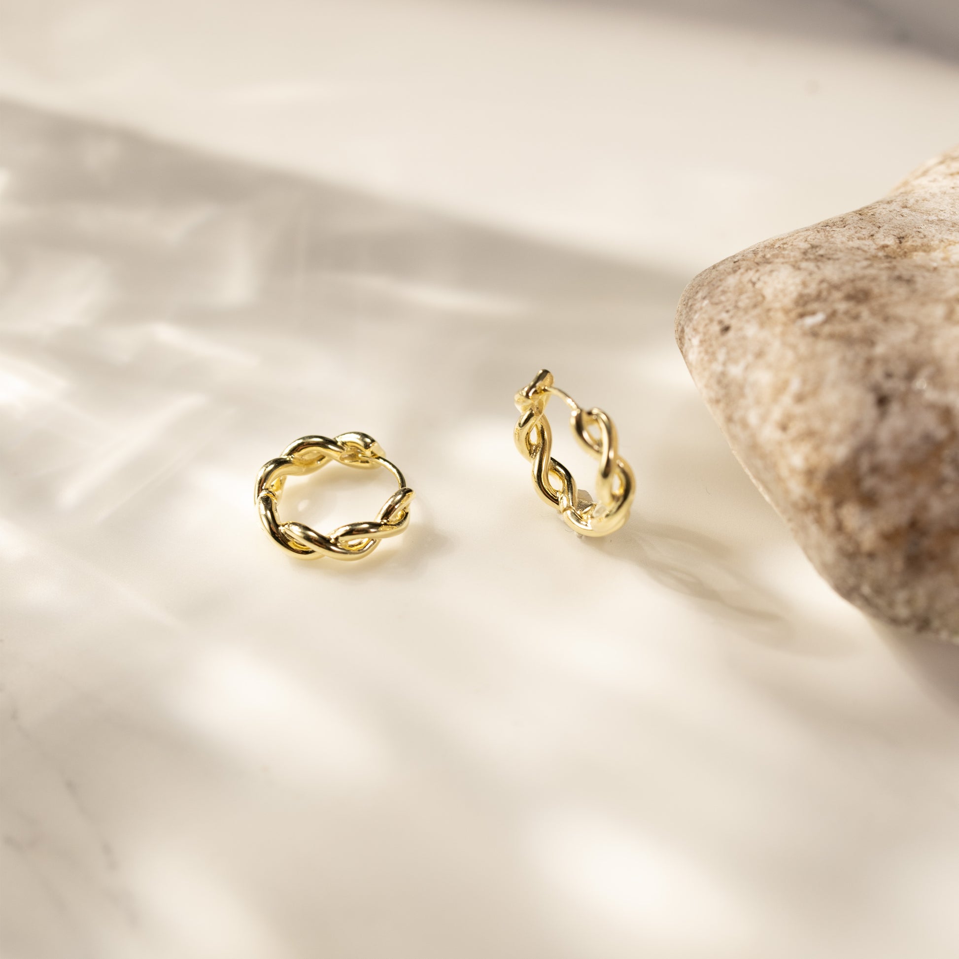 Eva 14K gold vermeil twisted link huggie earrings lifestyle scene on light stone background, reflective small gold hoops by Silvbreeze.