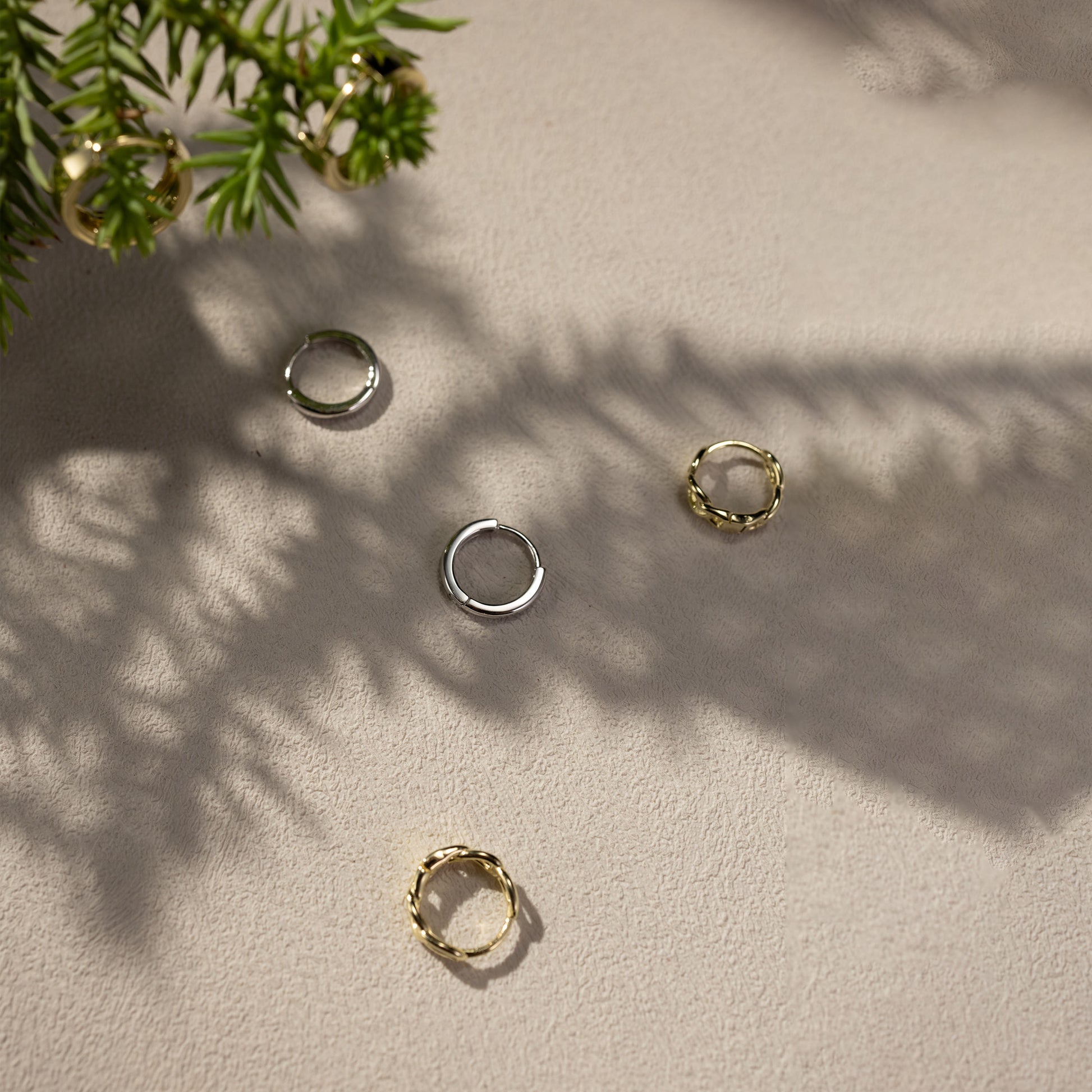 Lina smooth silver huggie earrings and Eva gold twisted link huggie earrings in a soft natural lifestyle scene, lightweight waterproof hypoallergenic everyday hoops by SILVBREEZE