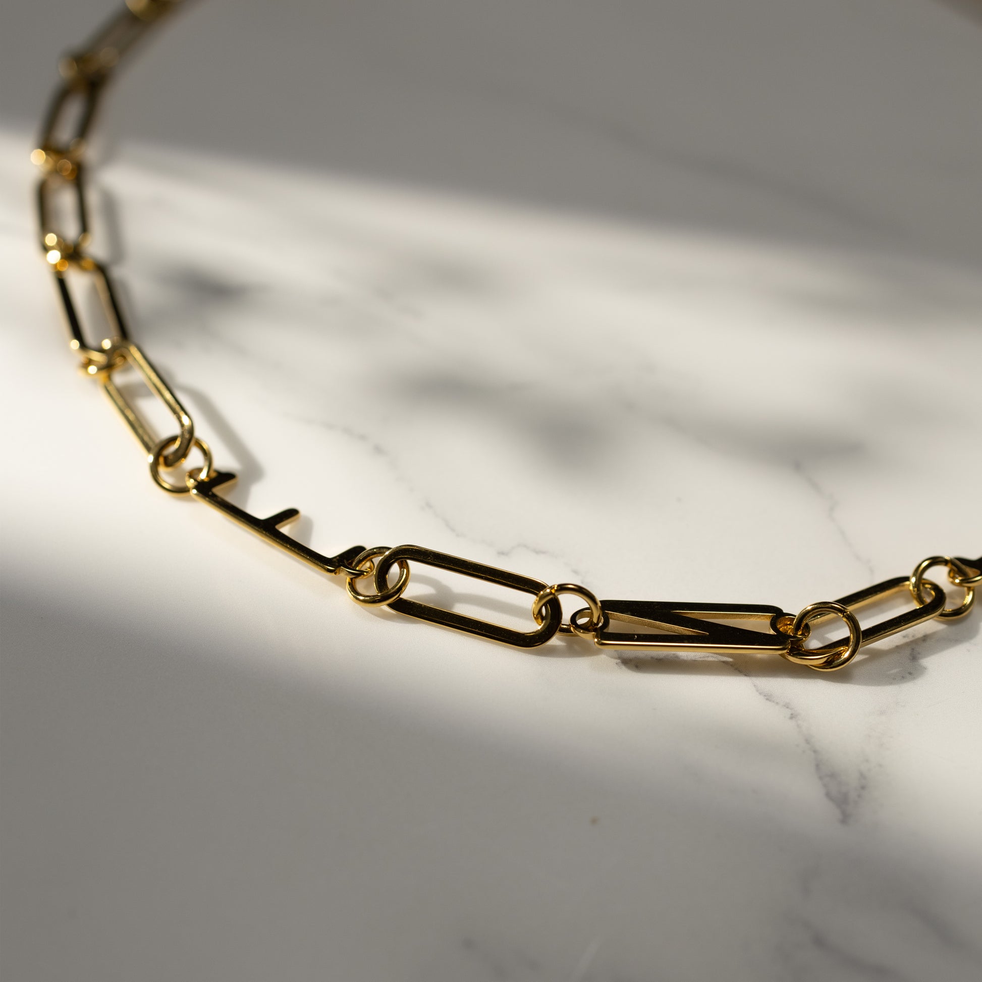Close-up of the gold MBTI letter necklace on a marble surface, featuring minimalist chain links and a durable 18K gold PVD finish.
