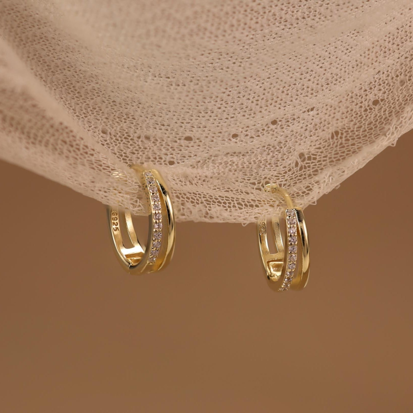 Nira gold vermeil huggie earrings hanging on lace fabric, sparkling cubic zirconia everyday hoops by Silvbreeze
