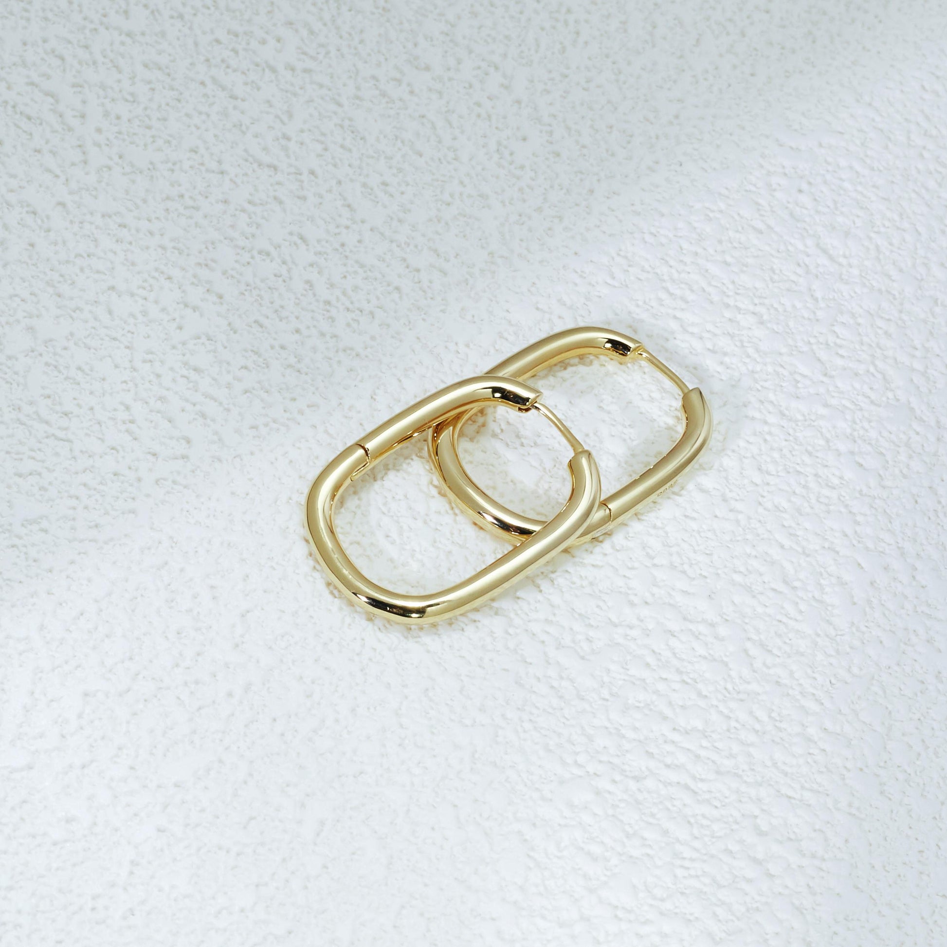Athena Oval Hoop Earrings – 14K Gold Plated Jewelry on Textured White Plaster Wall