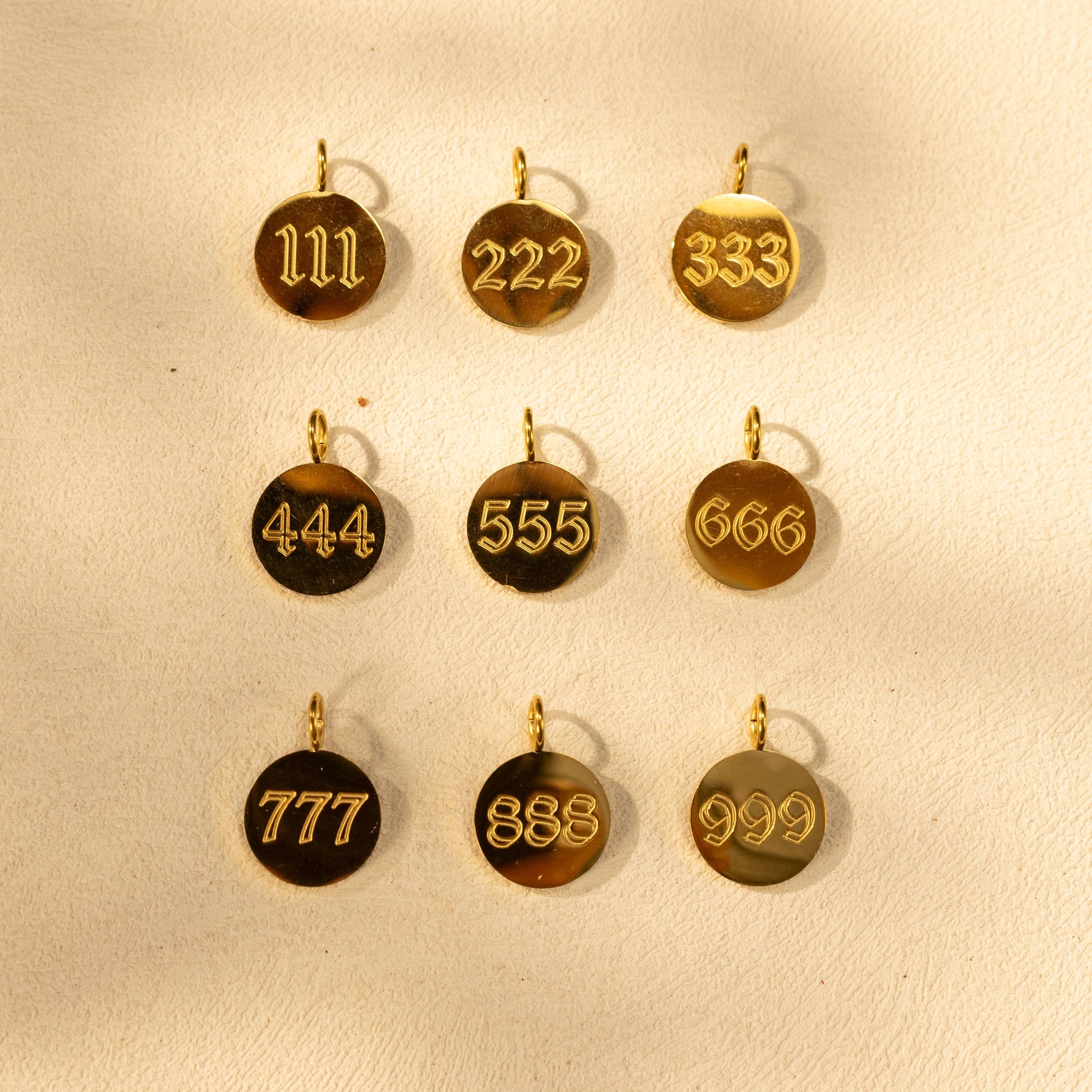 Silvbreeze gold angel number charms 111 to 999 displayed in a flatlay scene.