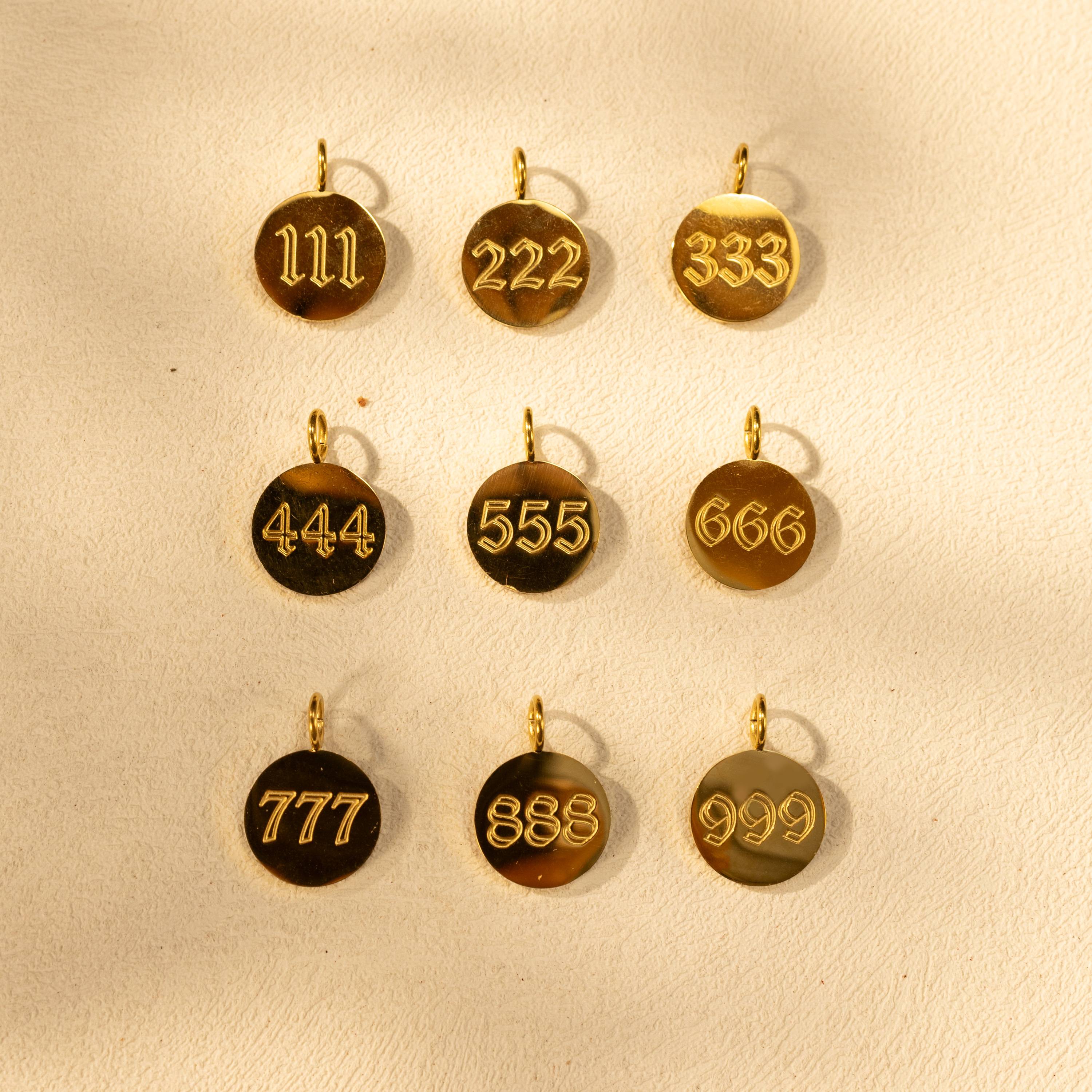 Silvbreeze gold angel number charms 111 to 999 displayed in a flatlay scene.