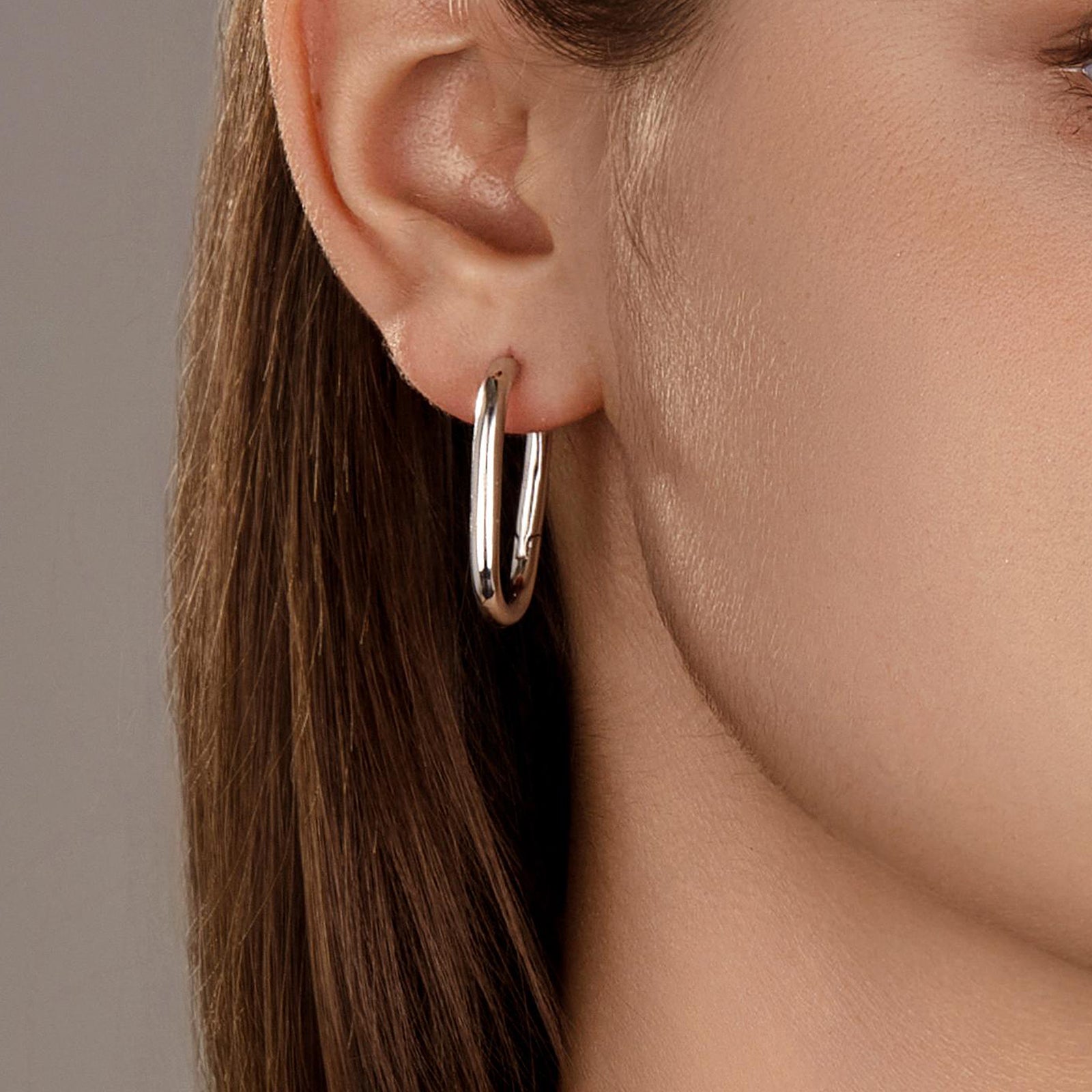 Close-up of model wearing the Silvbreeze Athena silver hoop earrings, highlighting the polished oval design.