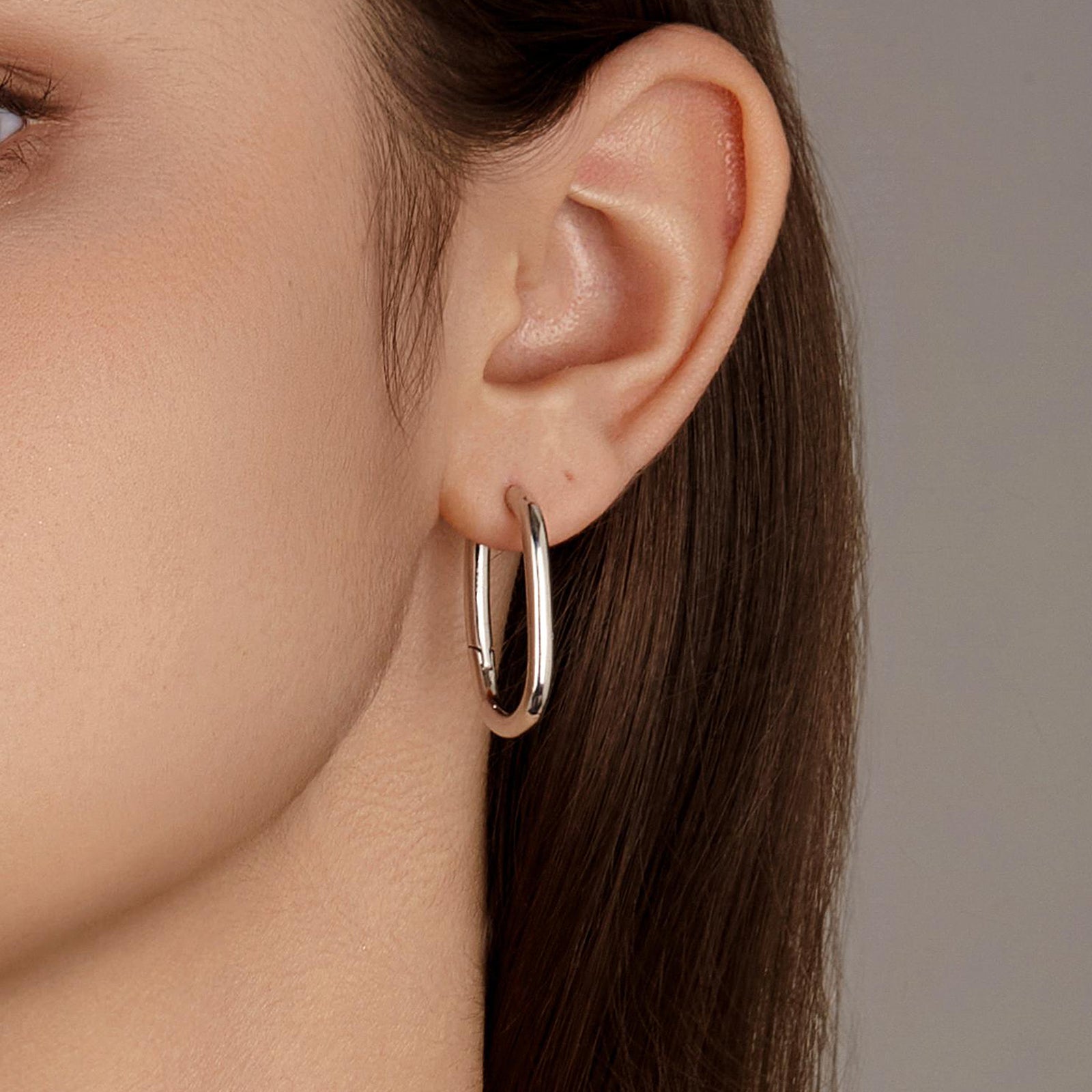 Close-up of model wearing the Silvbreeze Athena silver hoop earrings, showing the sleek oval silhouette and polished shine.
