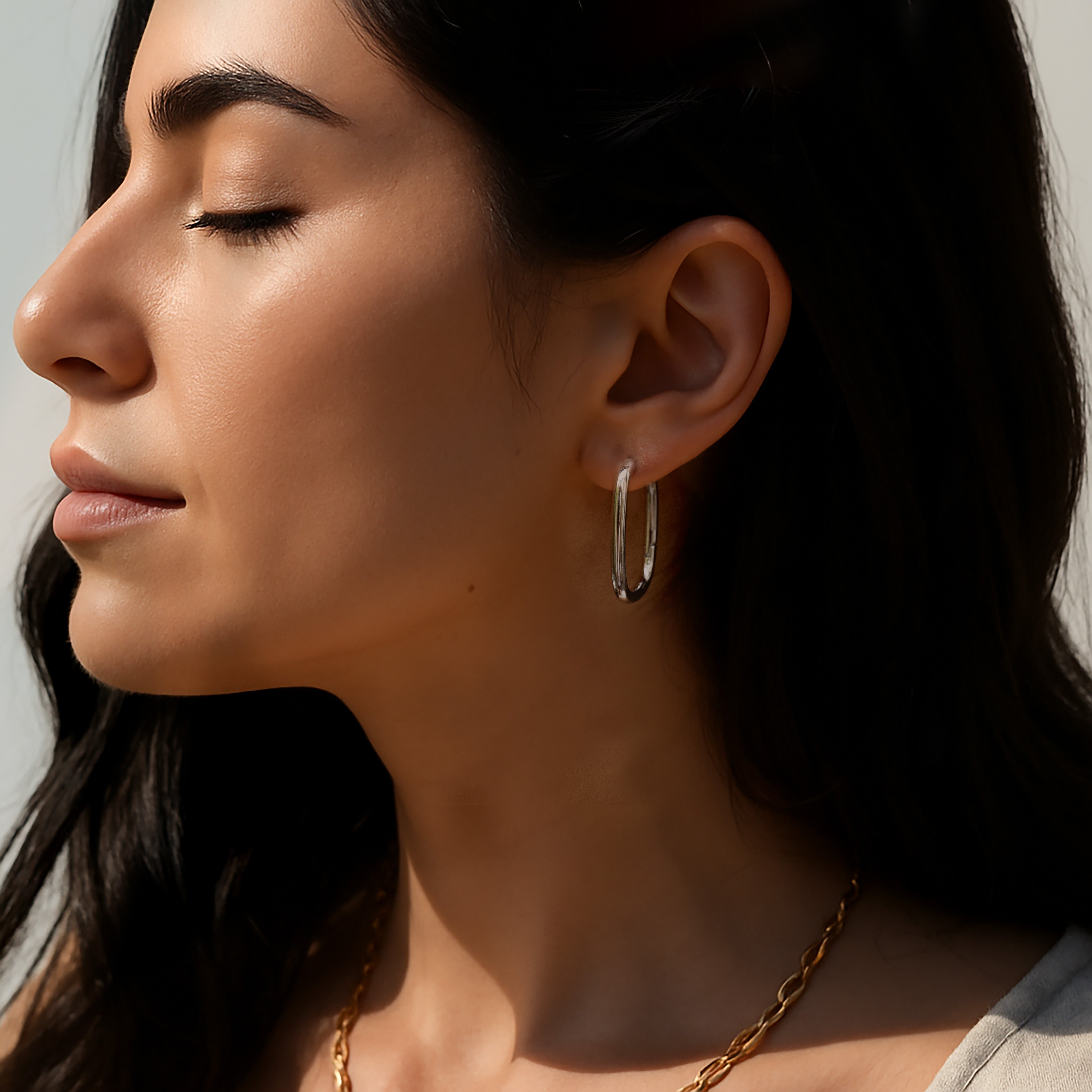 Model wearing the Silvbreeze Athena silver hoop earrings, showcasing the sleek oval design in soft natural light.