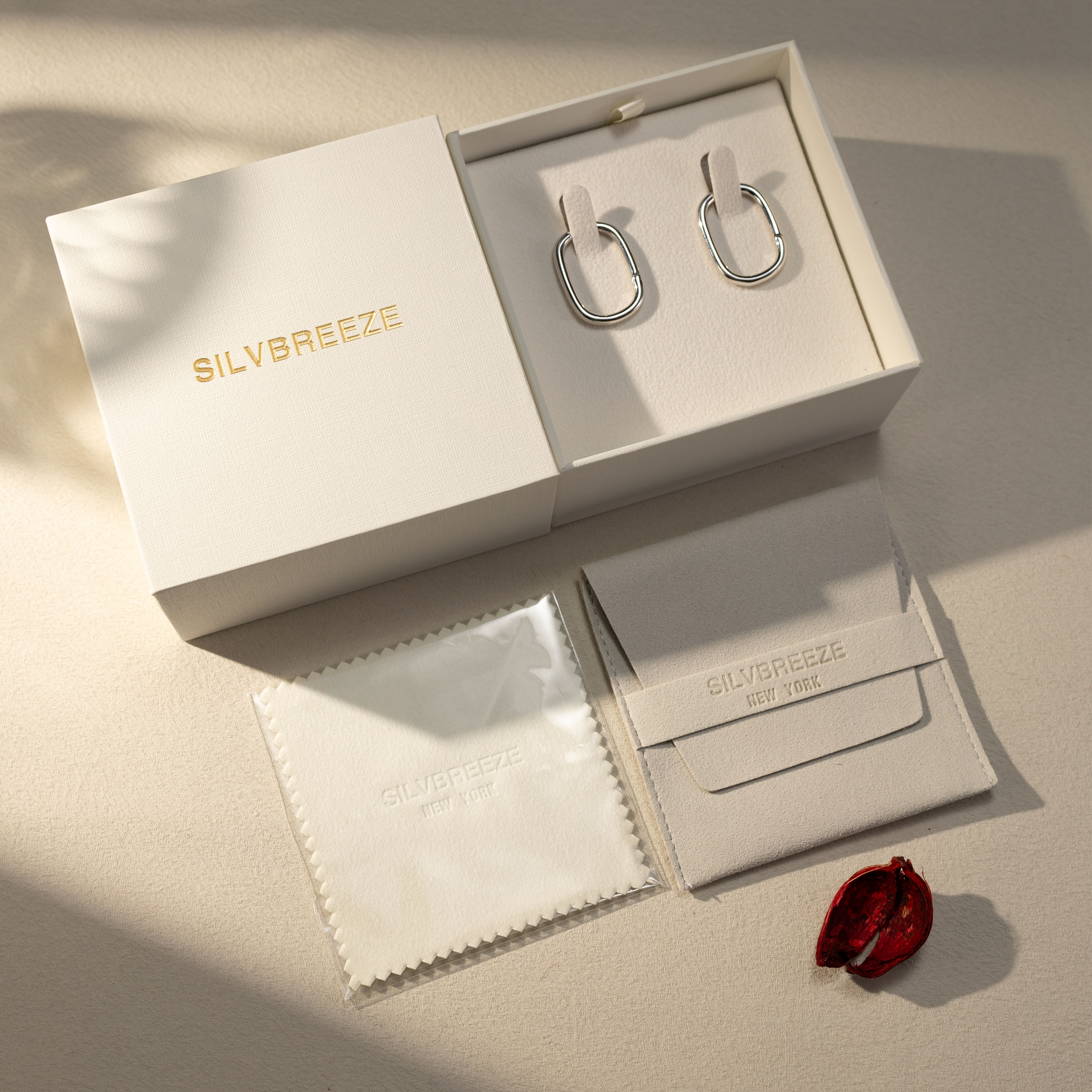 Silvbreeze Athena silver hoop earrings displayed in gift box packaging with suede pouch and polishing cloth under soft sunlight.