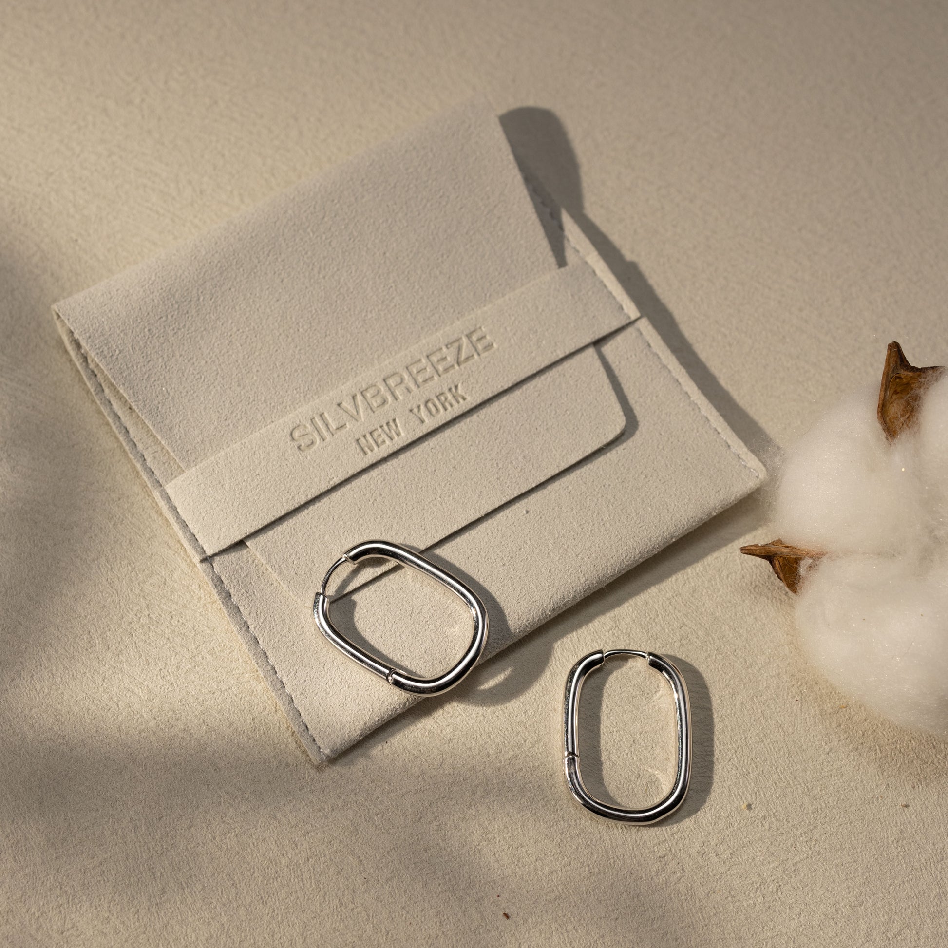 Silvbreeze Athena silver hoop earrings displayed beside a suede jewelry pouch under warm natural light.