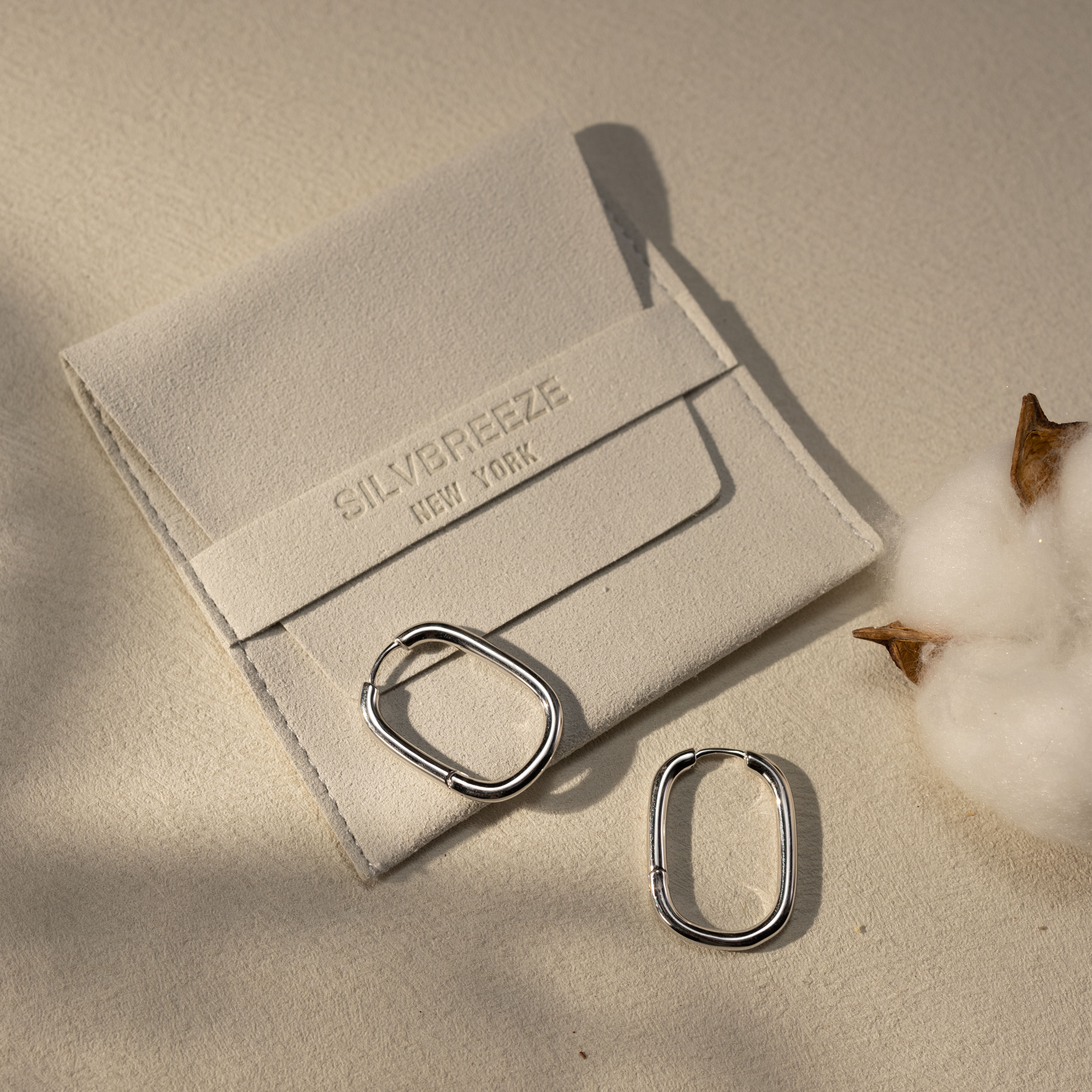 Silvbreeze Athena silver hoop earrings displayed beside a suede jewelry pouch under warm natural light.