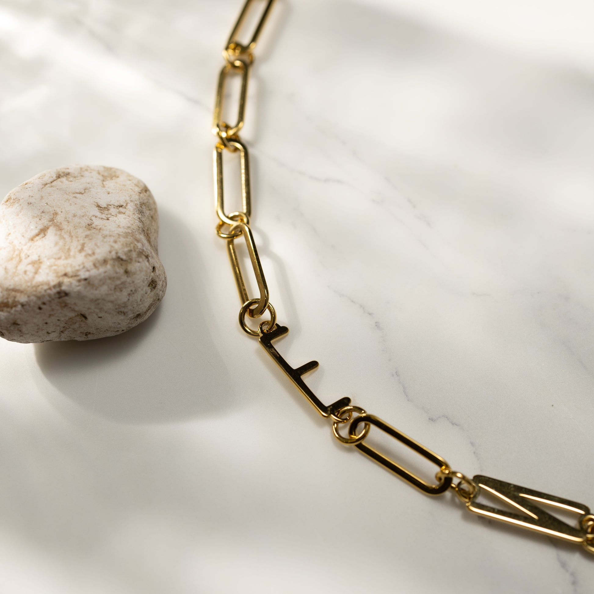 Closeup of the ENFP 18K gold paperclip chain necklace by Silvbreeze, styled on a marble surface with a natural stone accent under soft warm light.
