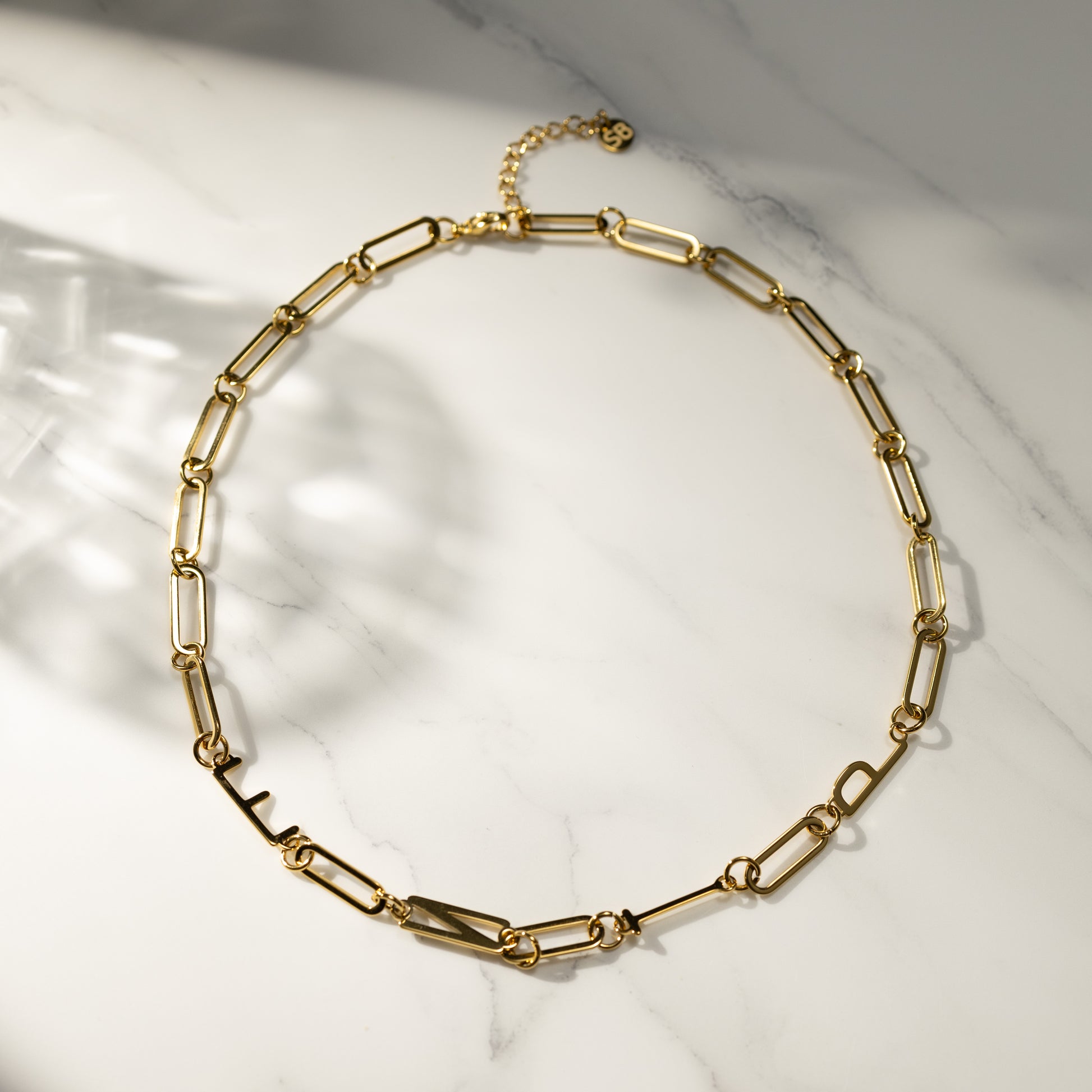 ENTP 18k gold paperclip chain necklace on marble background, circular layout, product detail shot.
