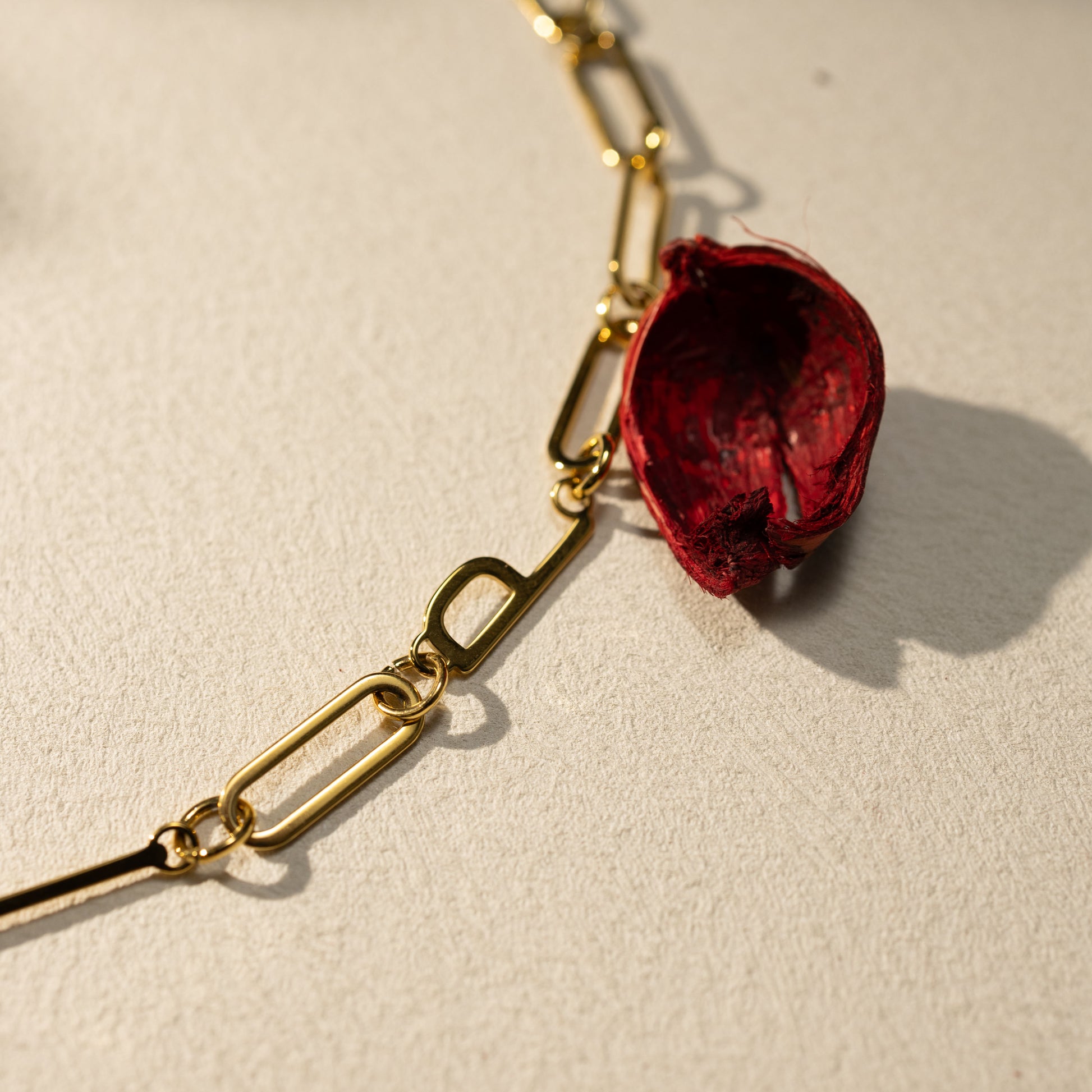 Closeup of the ESFP gold paperclip necklace pendant featuring the letter “P”, styled with a dried red petal on a soft neutral background, minimalist luxury aesthetic.