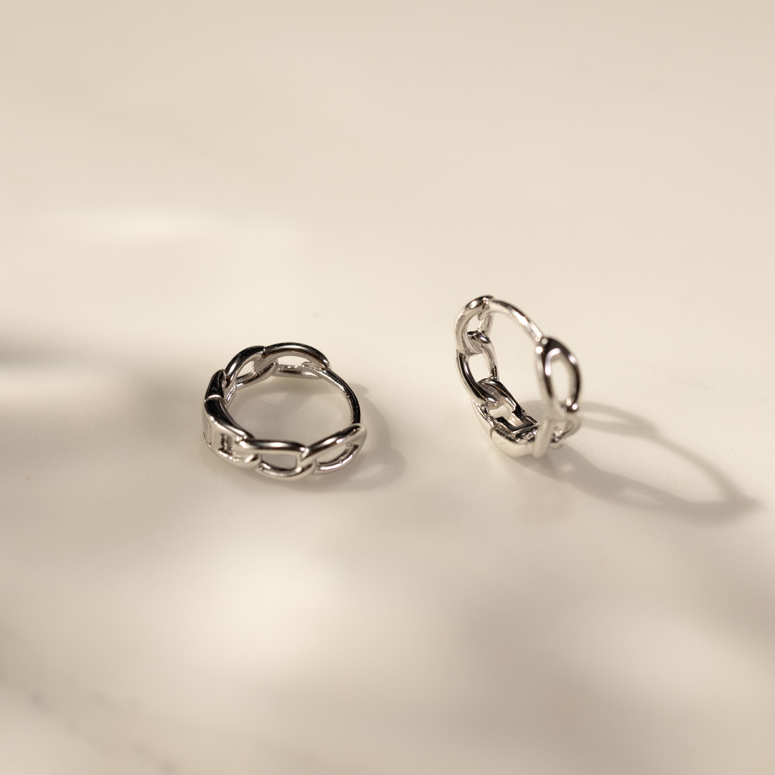 Eva twisted link huggie hoop earrings in white gold vermeil, crafted from solid sterling silver, shown as a pair on a clean minimal surface with soft warm light and shadow, modern waterproof everyday jewelry by SILVBREEZE