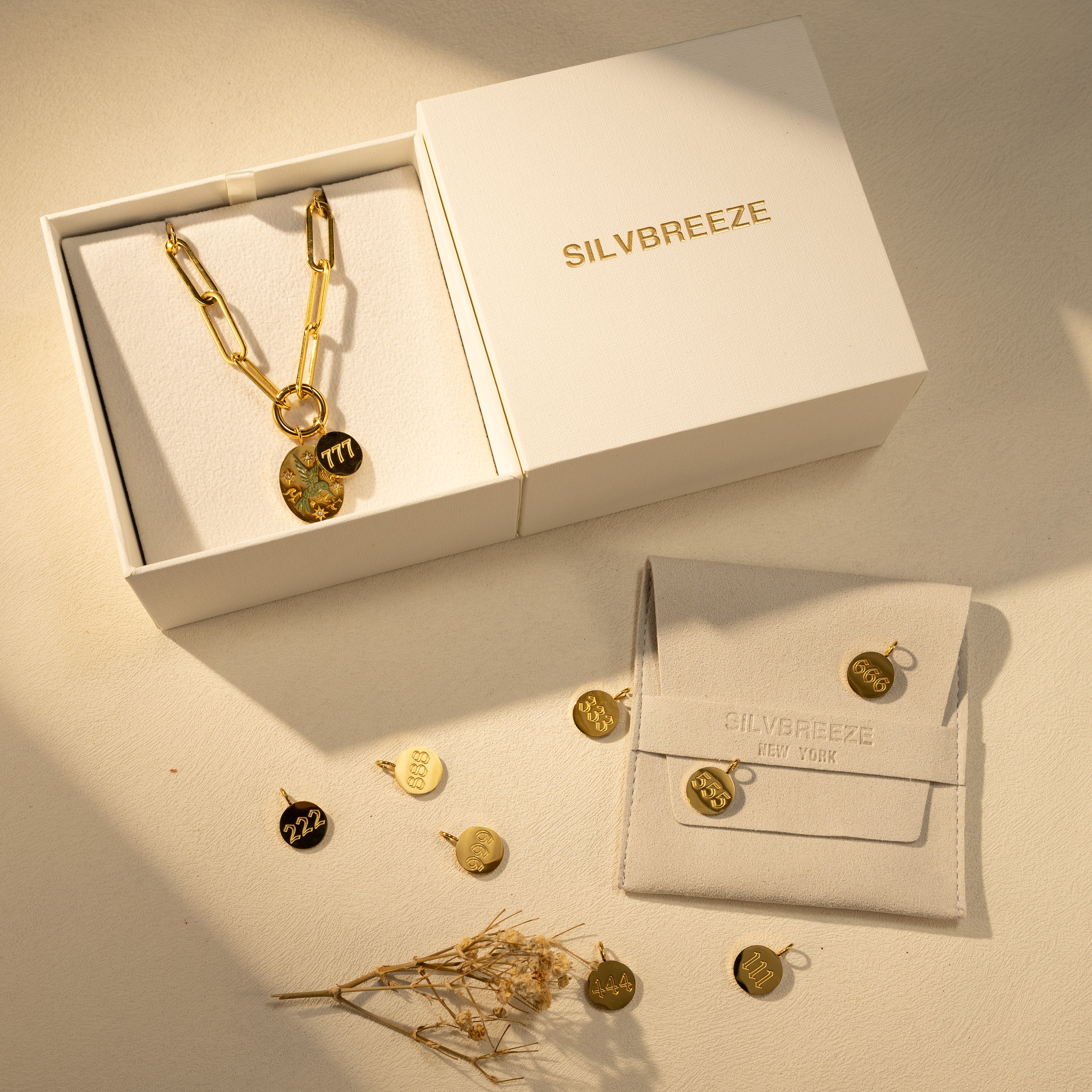 Gift packaging set with SILVBREEZE box and suede pouch, showing an 18K gold-plated paperclip O-clasp charm holder necklace with hand-painted green bird pendant and selectable angel number charms.