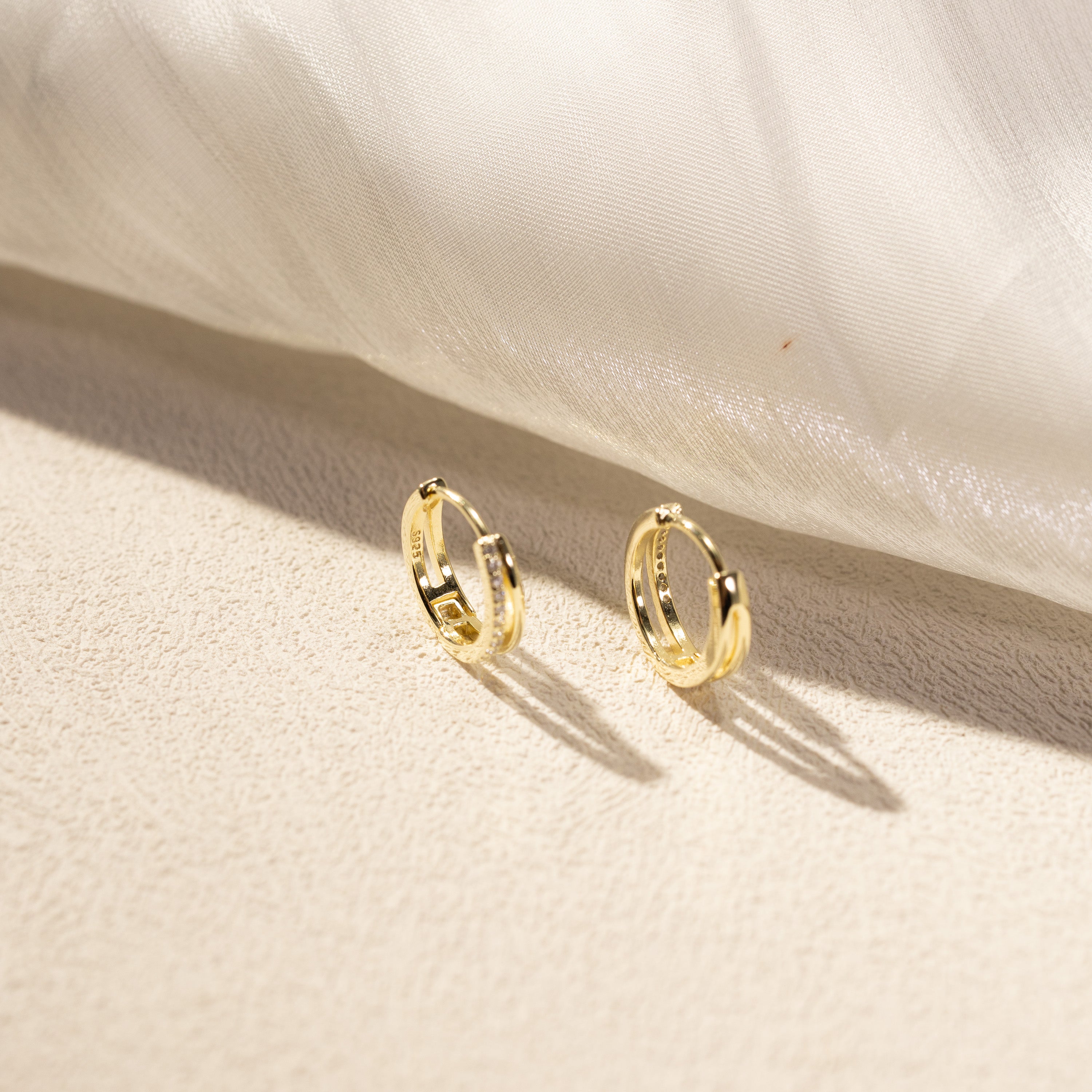 gold huggie hoop earrings with cubic zirconia pavé detail under soft fabric light, luxury jewelry lifestyle photography, Silvbreeze