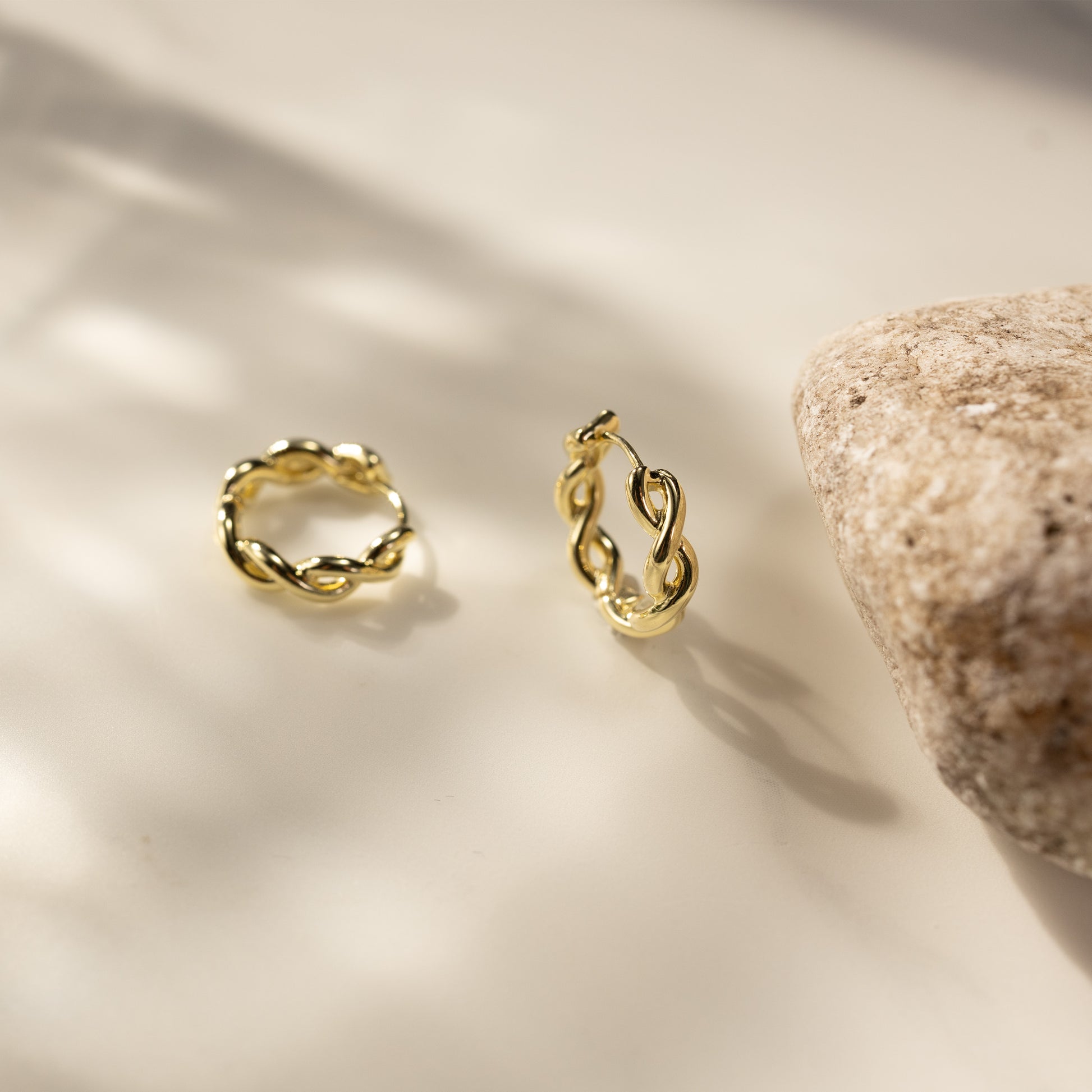 SILVBREEZE Kiva huggie hoop earrings in warm 14K gold vermeil shown in a soft lifestyle still scene, featuring twisted small hoop design with elegant shine and lightweight everyday style