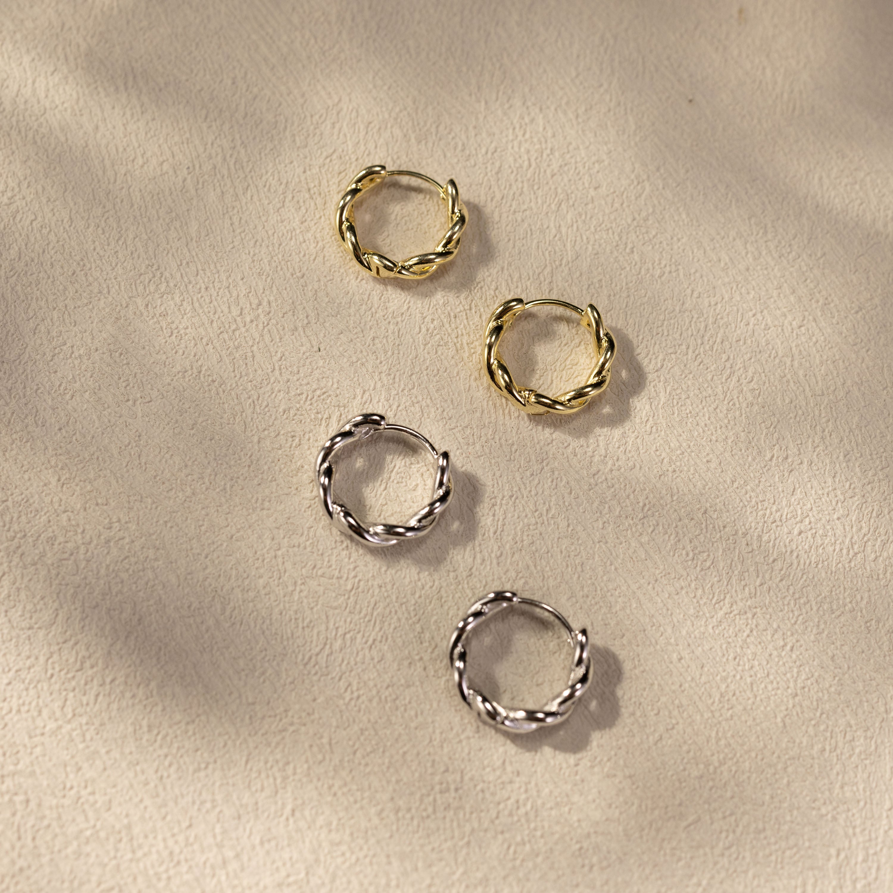 SILVBREEZE Kiva huggie hoop earrings in 14K gold vermeil and white gold vermeil shown together in a soft lifestyle scene, featuring twisted small hoop design with lightweight everyday shine