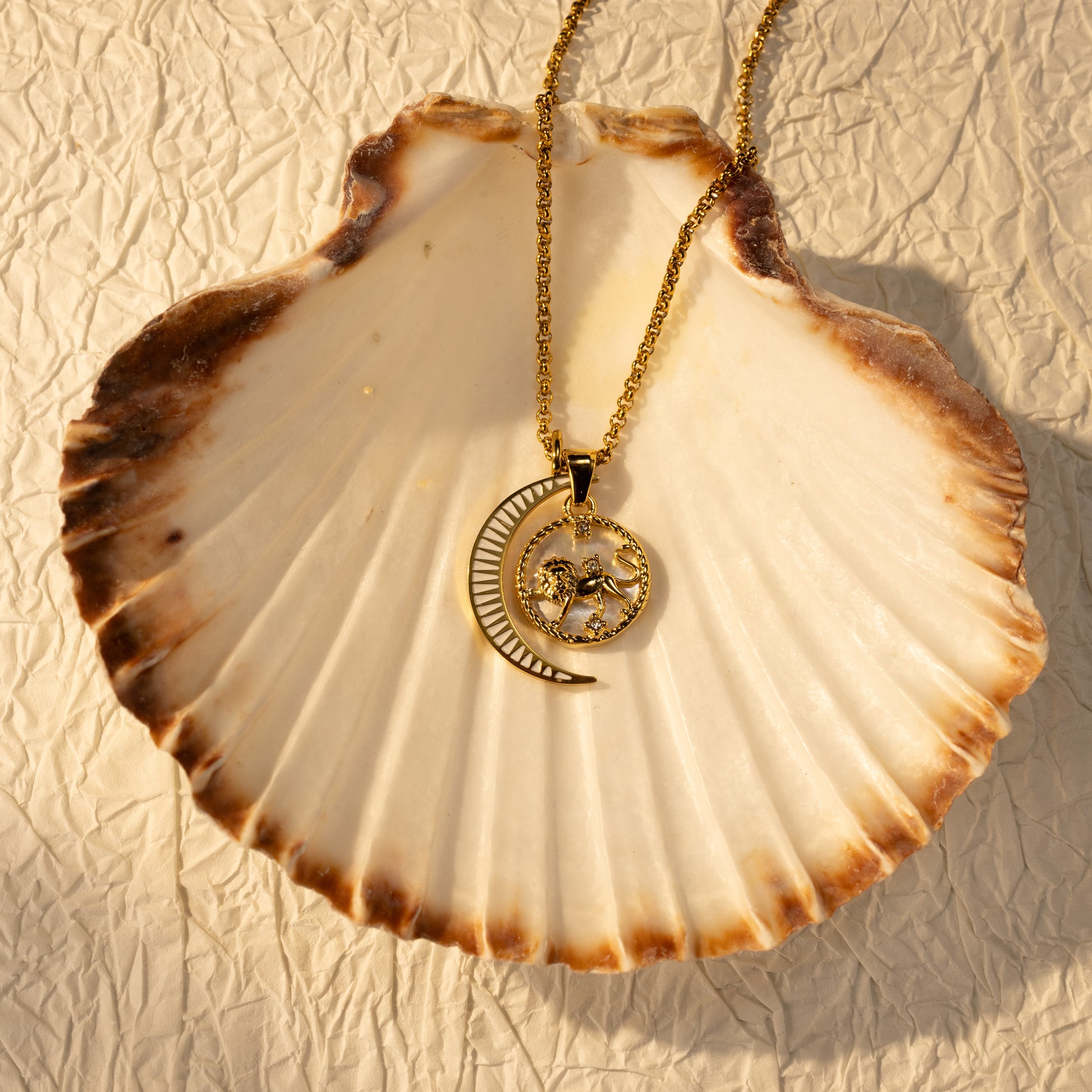 Silvbreeze Lunara Leo zodiac mother-of-pearl moon necklace with a rolo chain displayed on a seashell in warm sunlight.