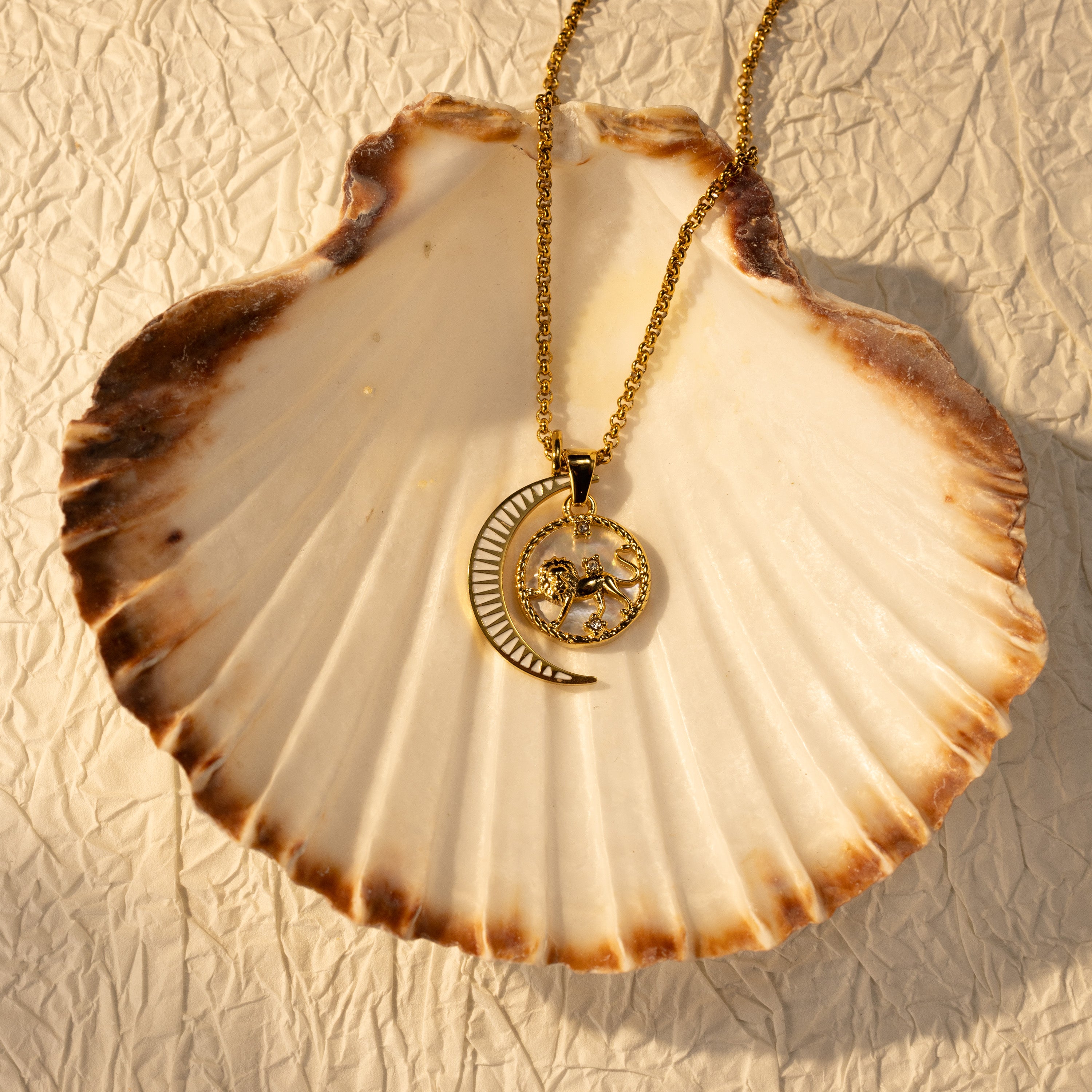 Silvbreeze Lunara Leo zodiac mother-of-pearl moon necklace with a rolo chain displayed on a seashell in warm sunlight.