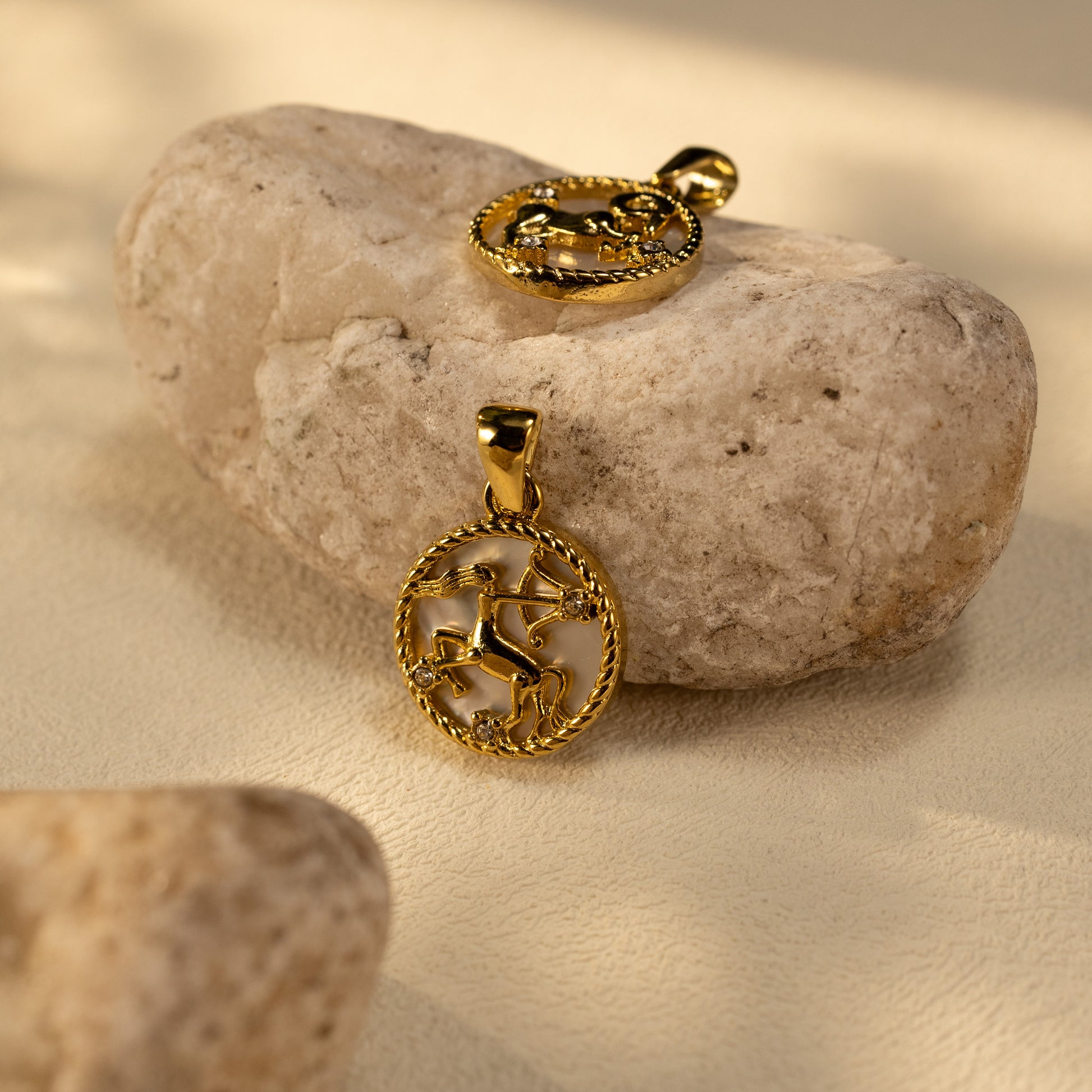 Silvbreeze Lunara Sagittarius and Capricorn zodiac mother-of-pearl pendants displayed on natural stone in warm sunlight.