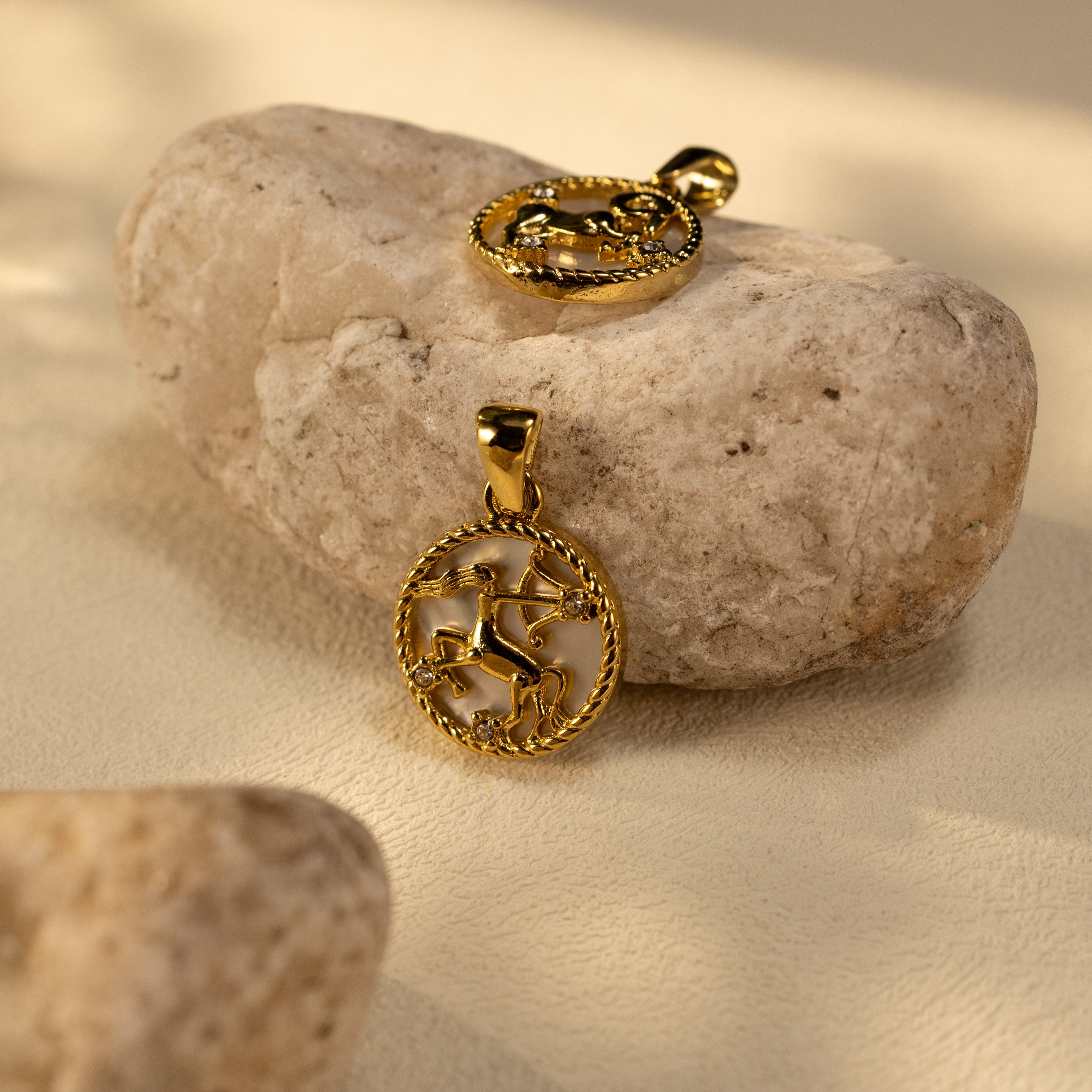 Silvbreeze Lunara Sagittarius and Capricorn zodiac mother-of-pearl pendants displayed on natural stone in warm sunlight.
