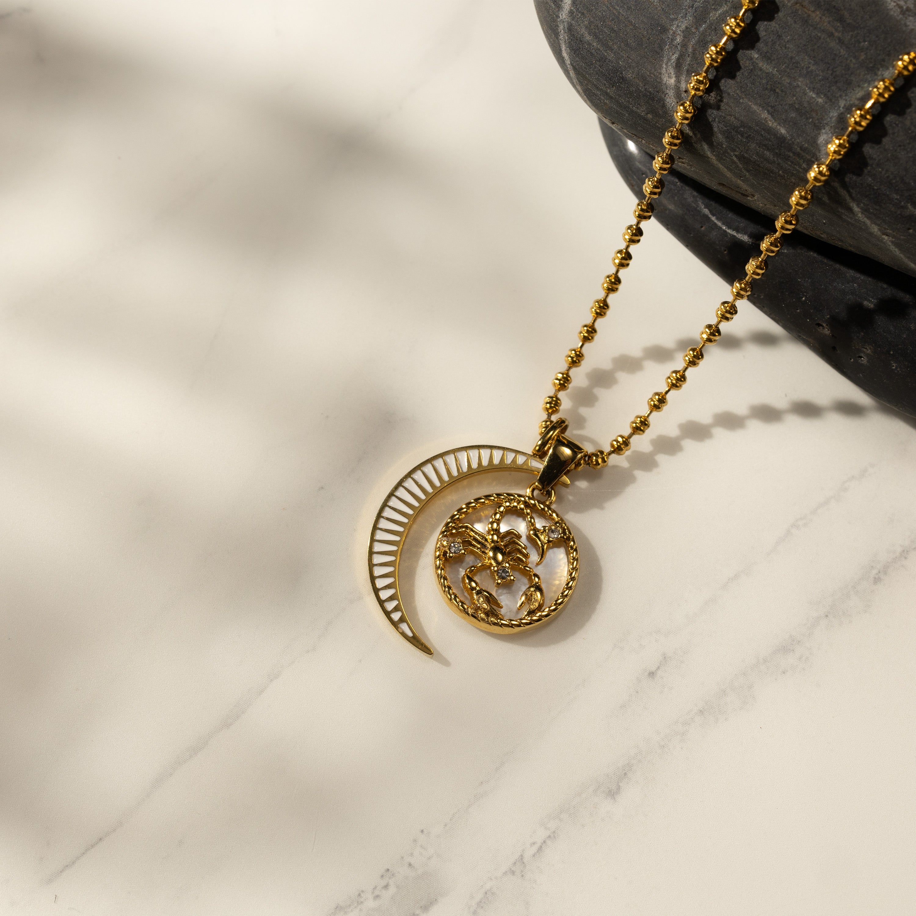 Silvbreeze Lunara Scorpio zodiac necklace with a gold bead chain and moon mother-of-pearl charm displayed on marble with soft shadows.