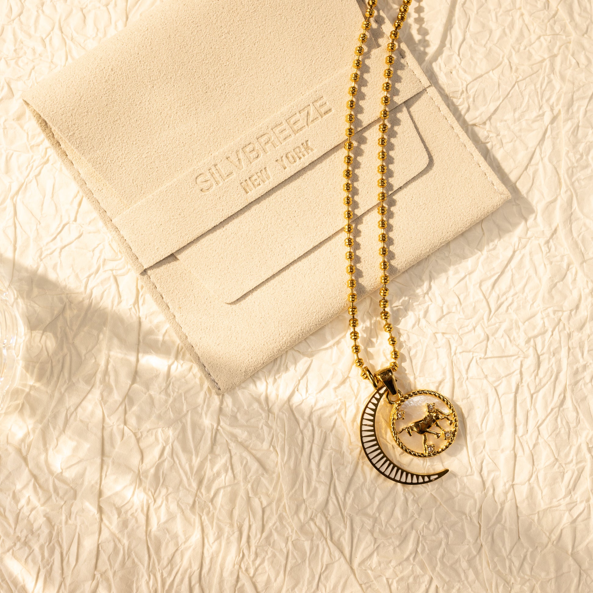 Silvbreeze Lunara Taurus zodiac necklace with bead chain and moon mother-of-pearl pendant displayed on a beige suede pouch.