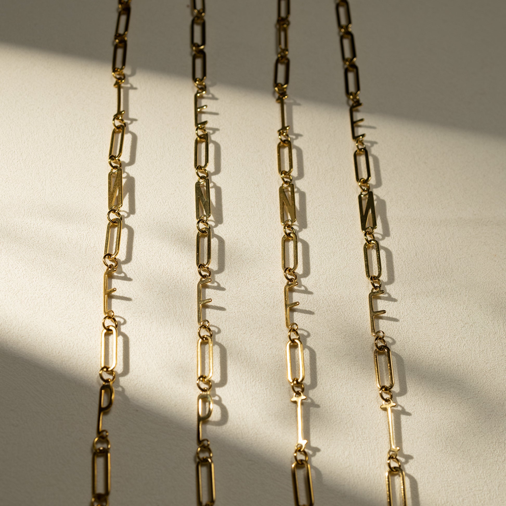 Silvbreeze MBTI 18K gold paperclip chain necklaces featuring INFP, ENFP, INFJ, and ENFJ letters displayed in a vertical lineup under warm natural sunlight on a beige textured surface.