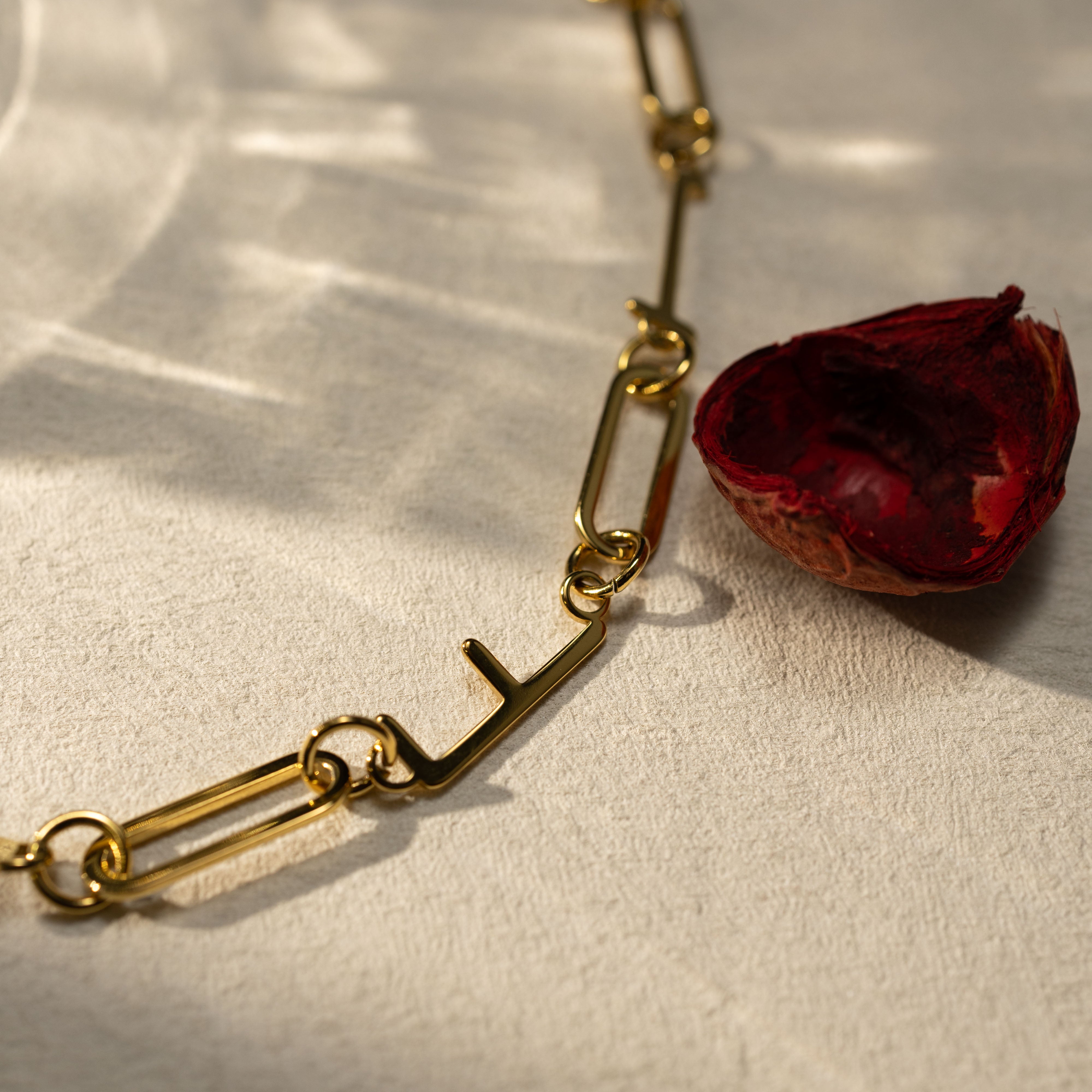 Closeup detail of a 18k gold paperclip chain necklace with a warm natural light shadow and soft texture background, Silvbreeze jewelry photography.