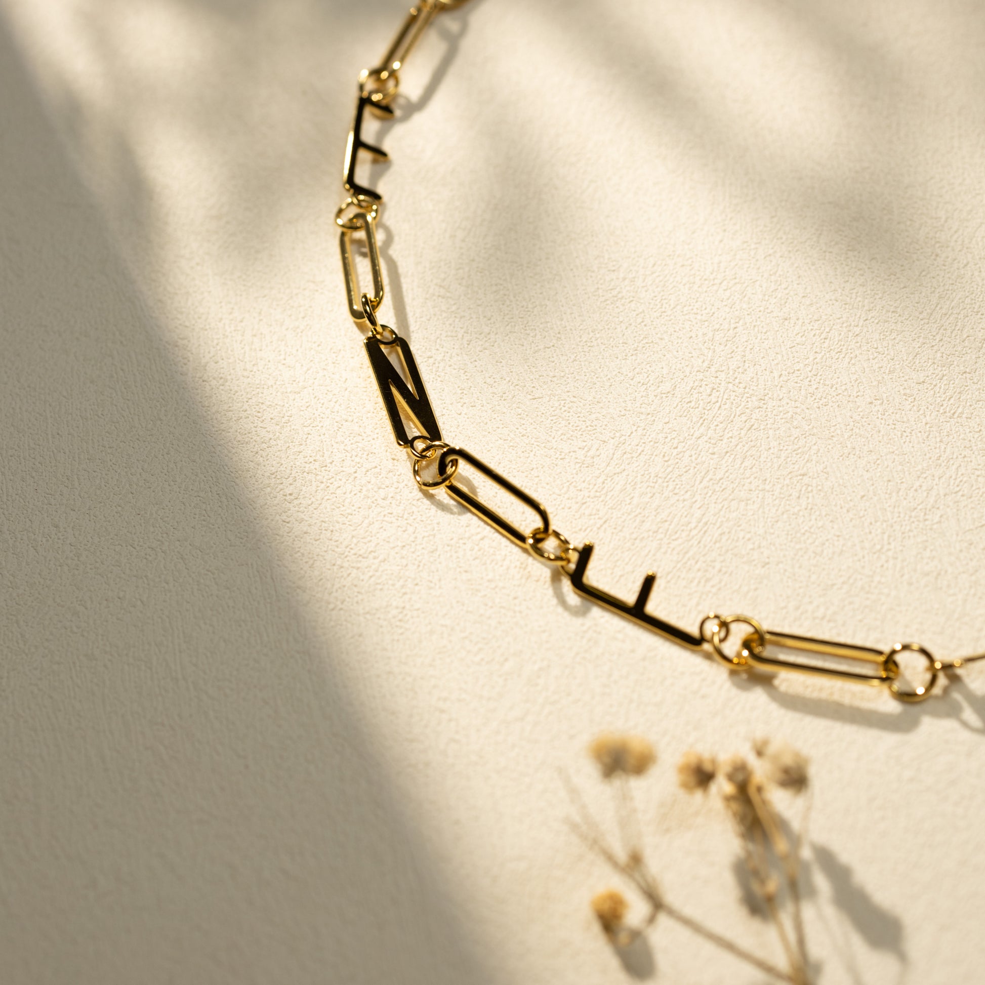 Closeup of Silvbreeze 18K gold MBTI paperclip chain necklace shot in warm natural light with dried floral accents, highlighting texture and shine.