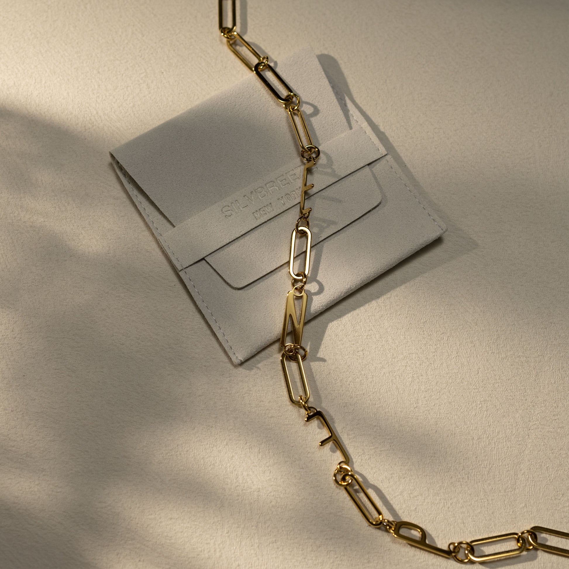 ENFP MBTI 18K gold plated paperclip chain necklace displayed on a Silvbreeze suede jewelry pouch under warm natural light.