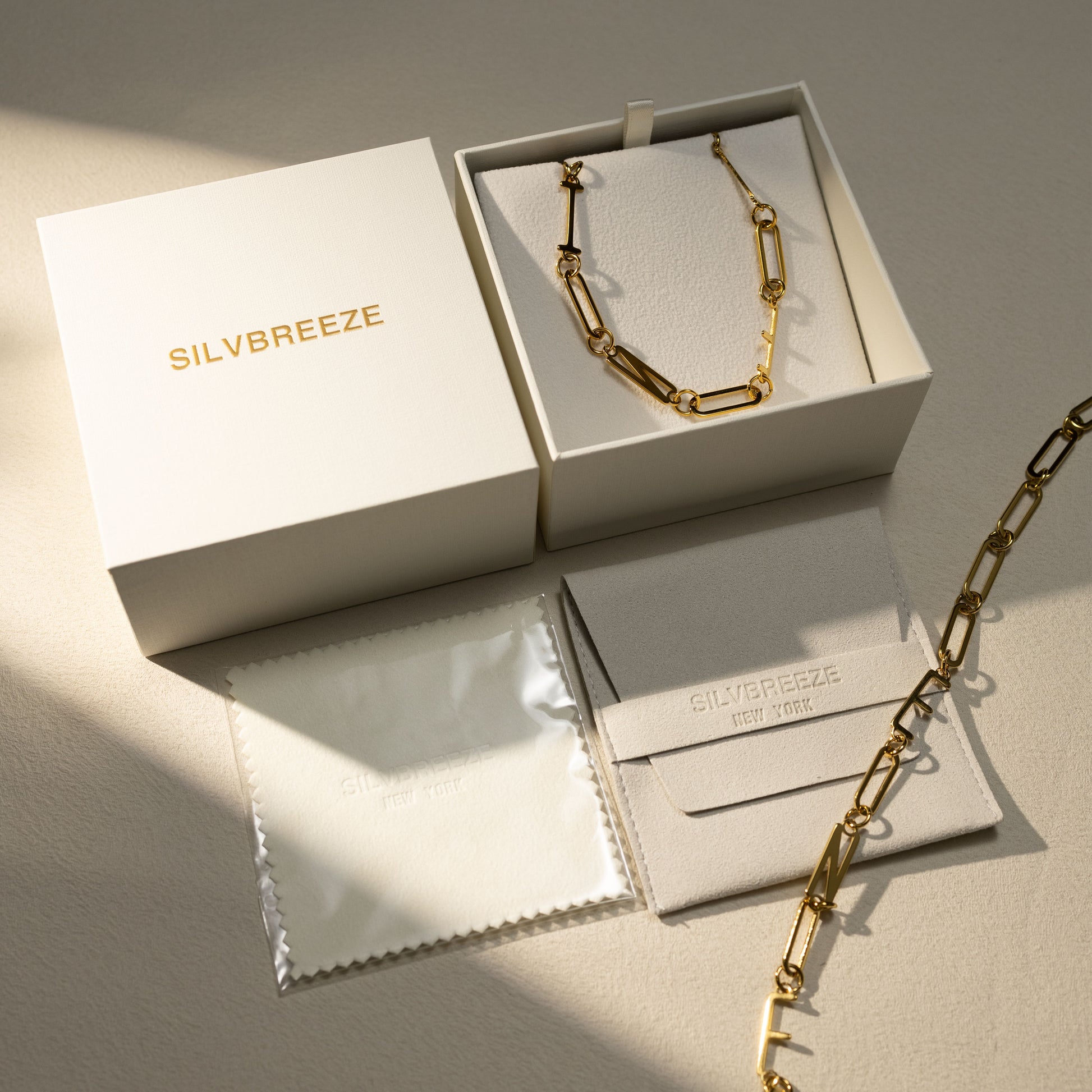 Silvbreeze 18K gold MBTI paperclip chain necklace displayed in an open gift box with branded jewelry pouch and polishing cloth in a soft warm flatlay packaging scene.