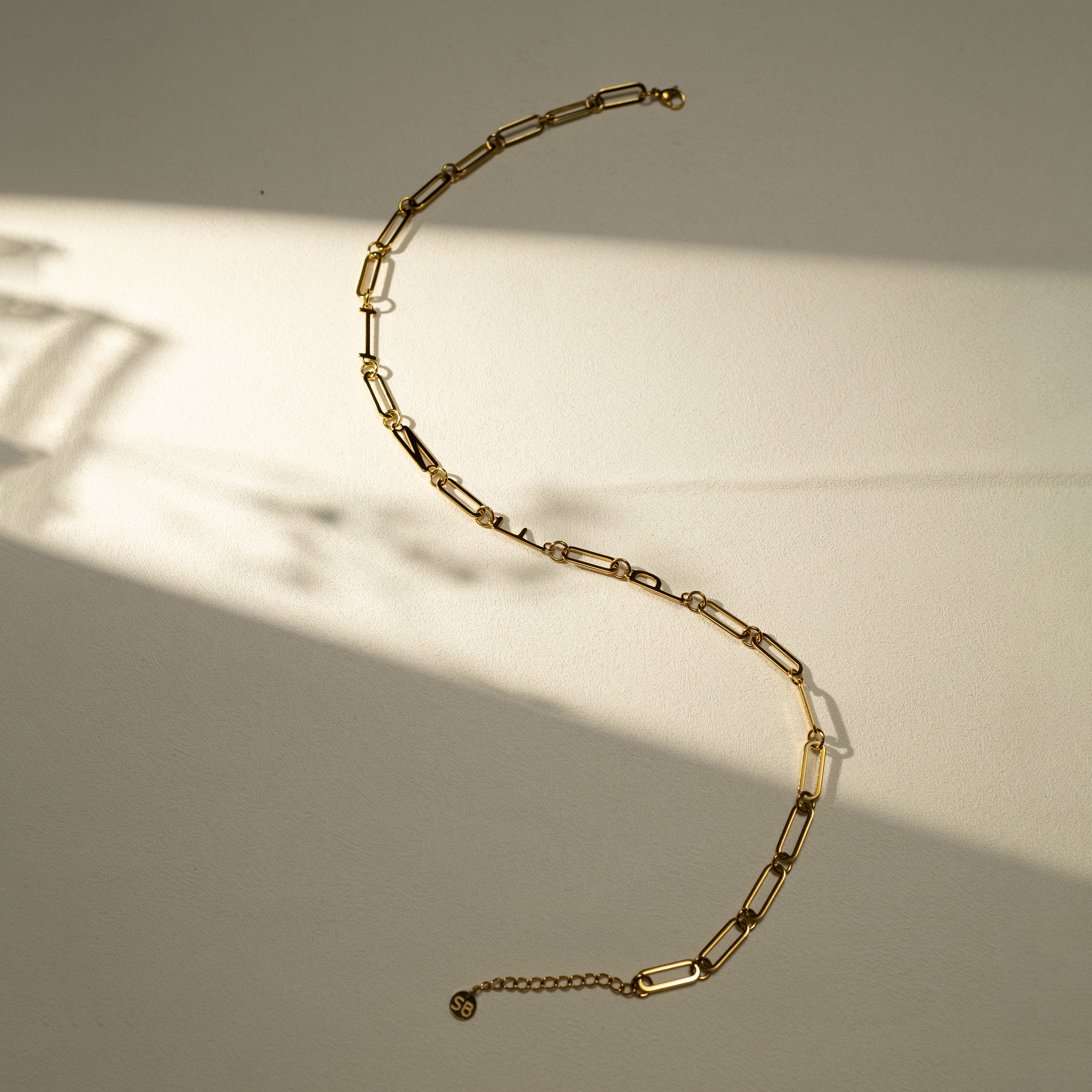 INFP 18K gold personality necklace with 18K gold PVD finish displayed in a warm soft-shadow aesthetic scene, featuring paperclip chain and SB brand tag.