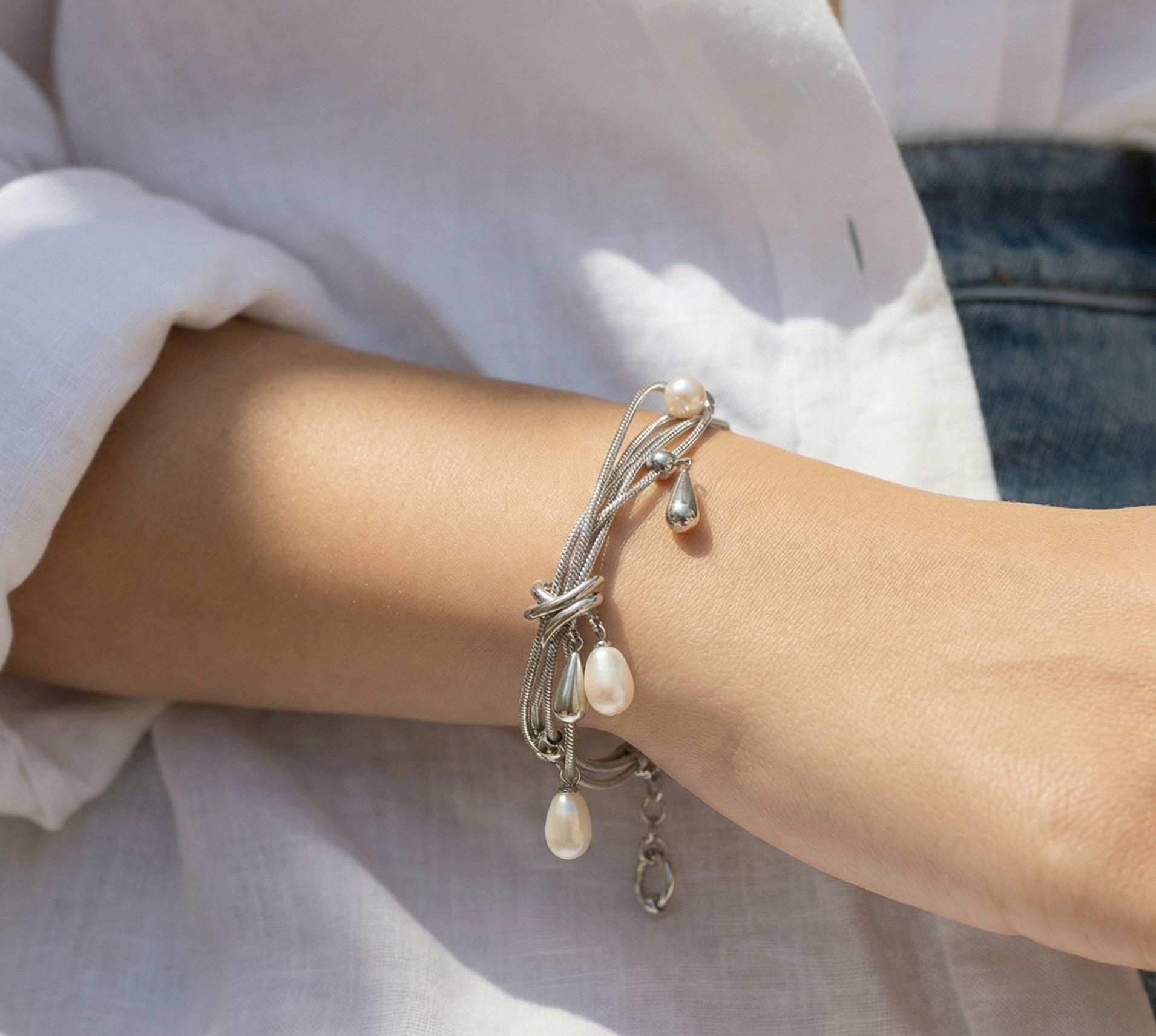 Model wearing Silvbreeze NORN mother of pearl five fate snake chain bracelet, styled on the wrist with a layered silver chain look