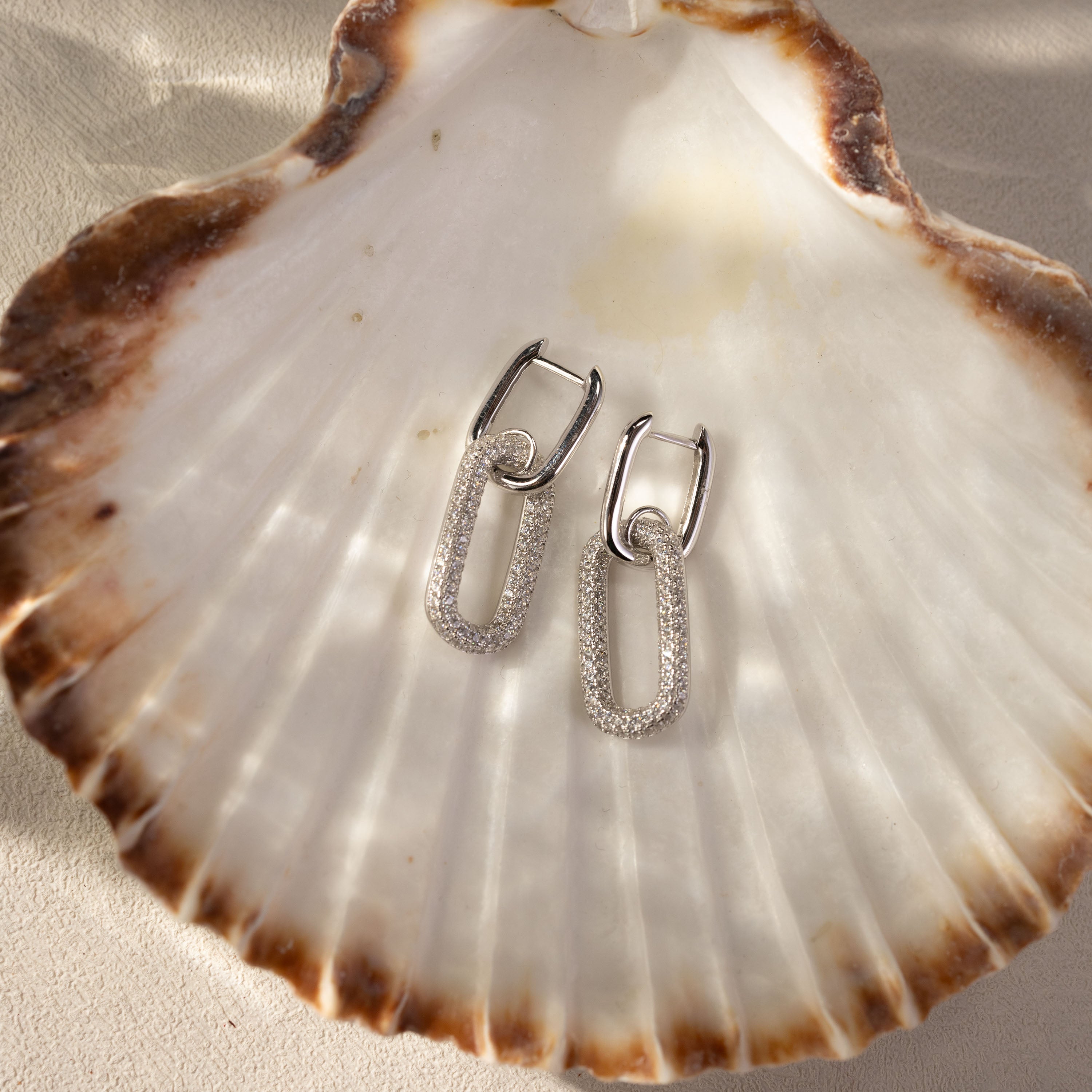 Silvbreeze Ona Paperclip Drop Earrings displayed on natural seashell – pavé oval link design.