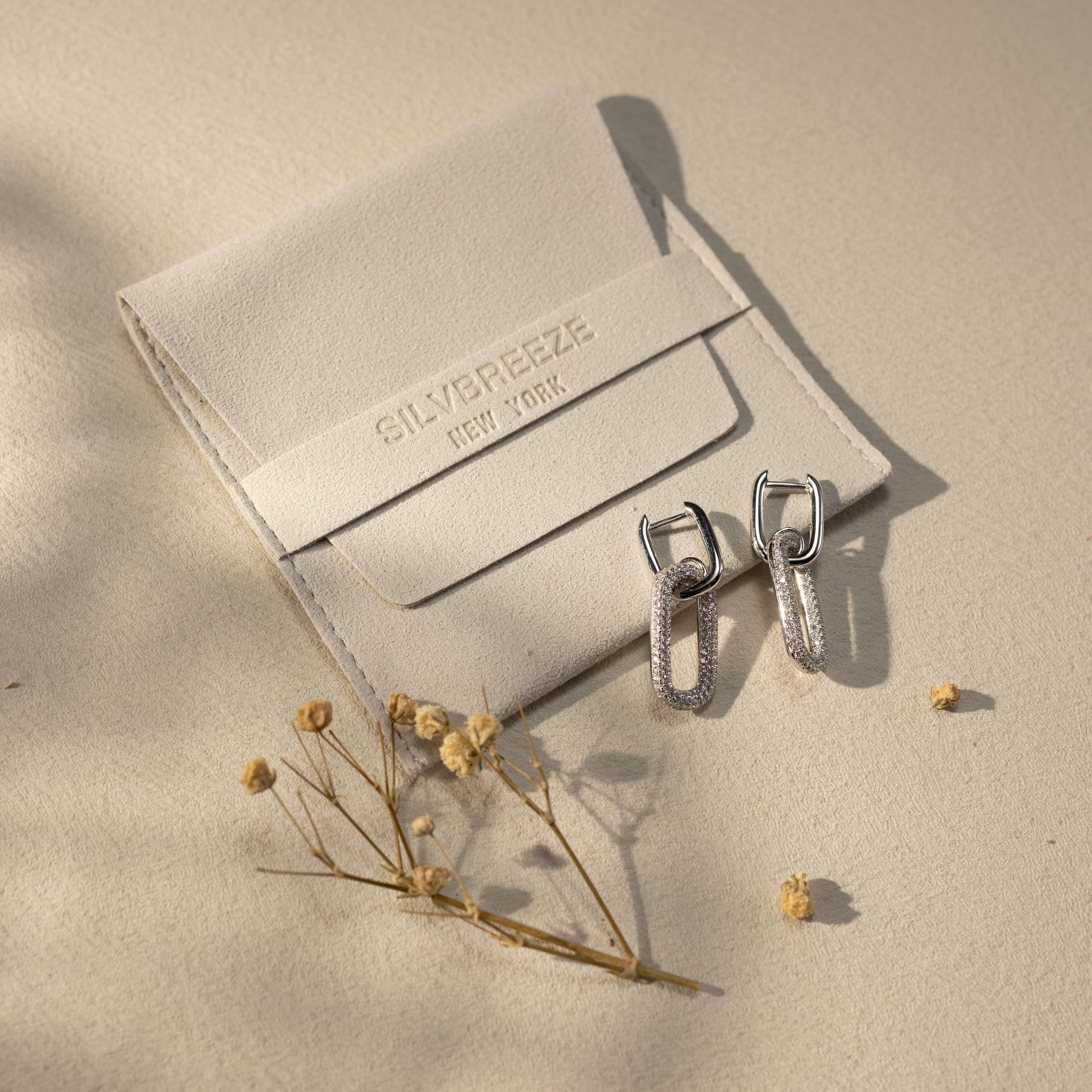 Silvbreeze Ona Paperclip Drop Earrings displayed with signature suede pouch, soft beige flatlay scene.