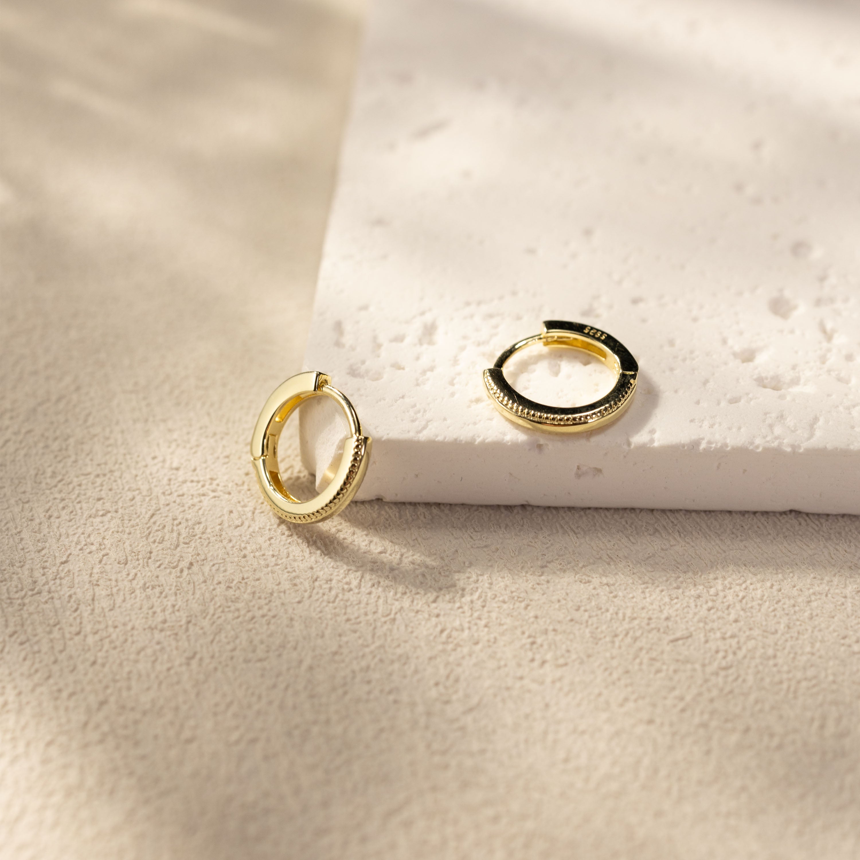 Onita gold vermeil huggie earrings on textured stone surface, small sterling silver hoops with sculpted edge detailing by SILVBREEZE