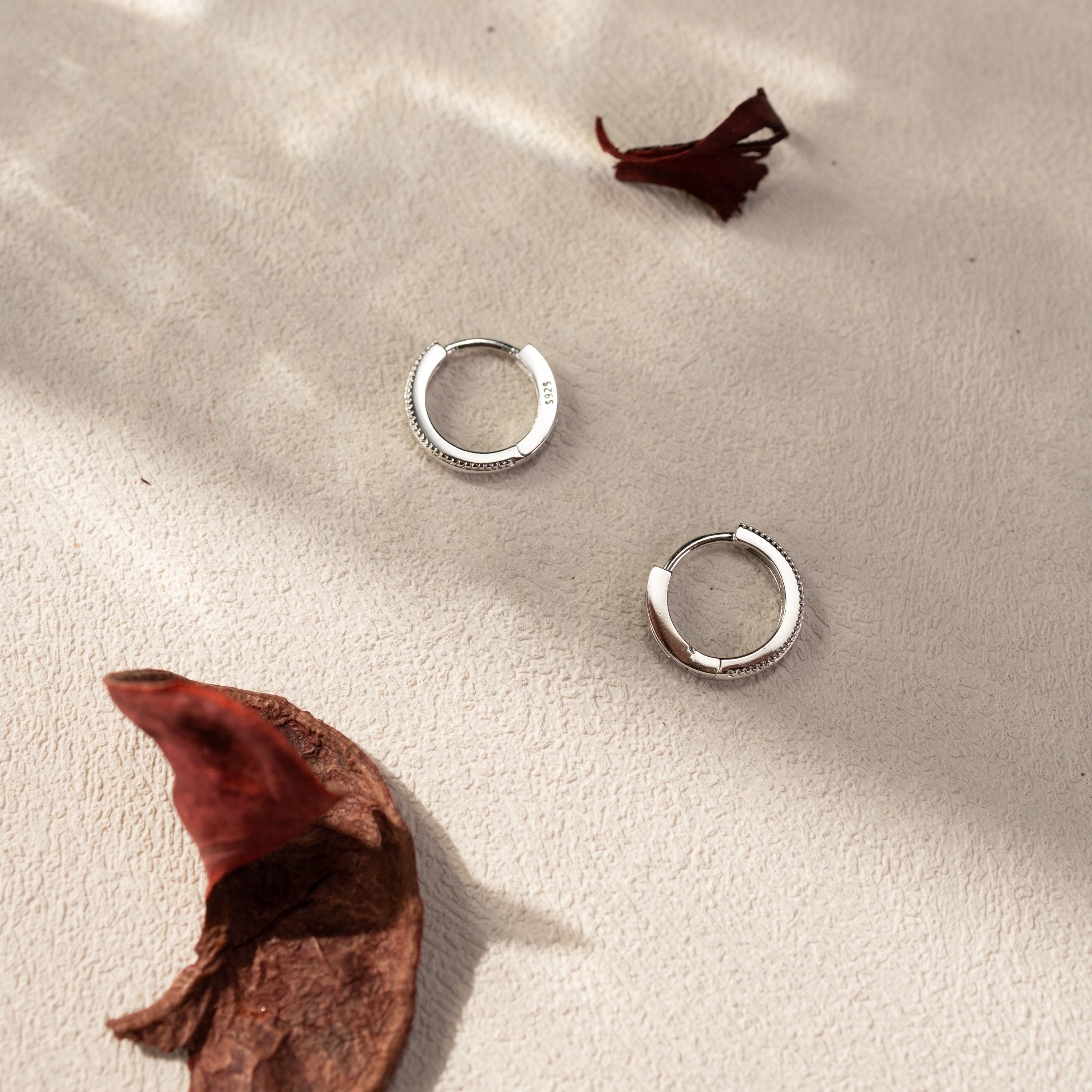 Onita white gold vermeil huggie earrings flatlay on textured surface, lightweight tarnish-resistant hoop earrings by Silvbreeze
