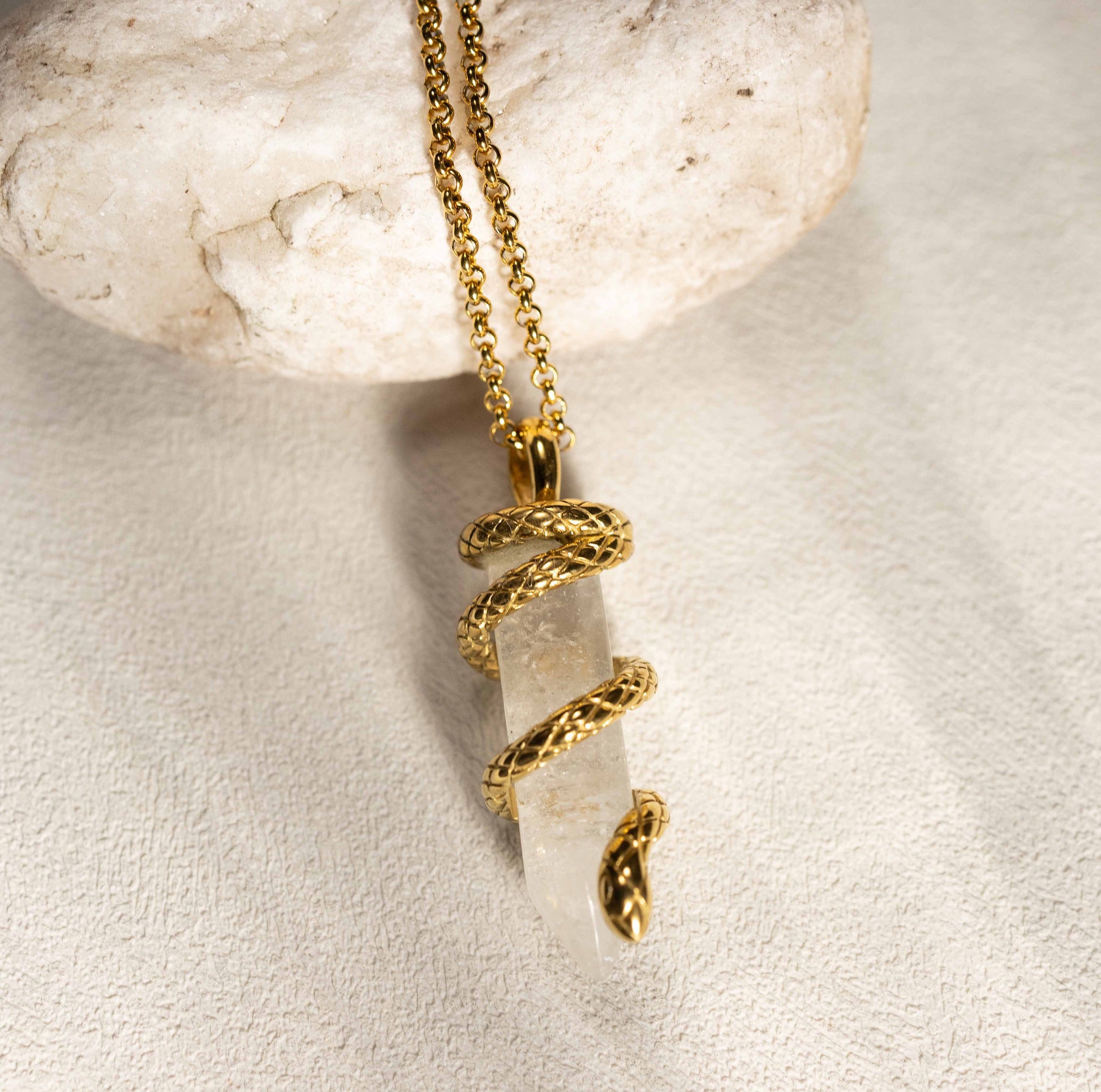 Silvbreeze Ouroboros serpent clear quartz necklace styled on natural stone, emphasizing the crystal’s clarity and the gold serpent wrap