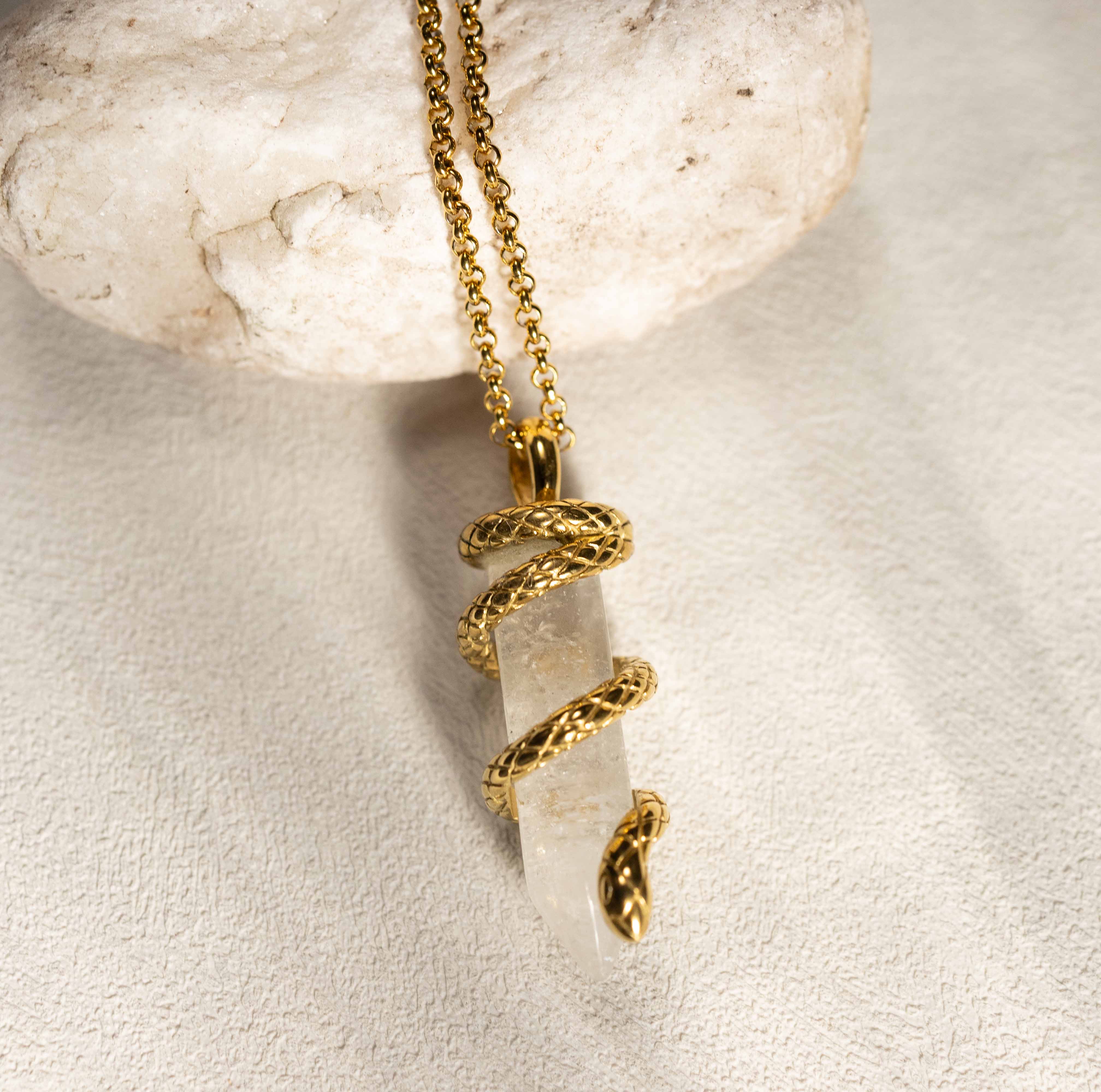 Silvbreeze Ouroboros serpent clear quartz necklace styled on natural stone, emphasizing the crystal’s clarity and the gold serpent wrap