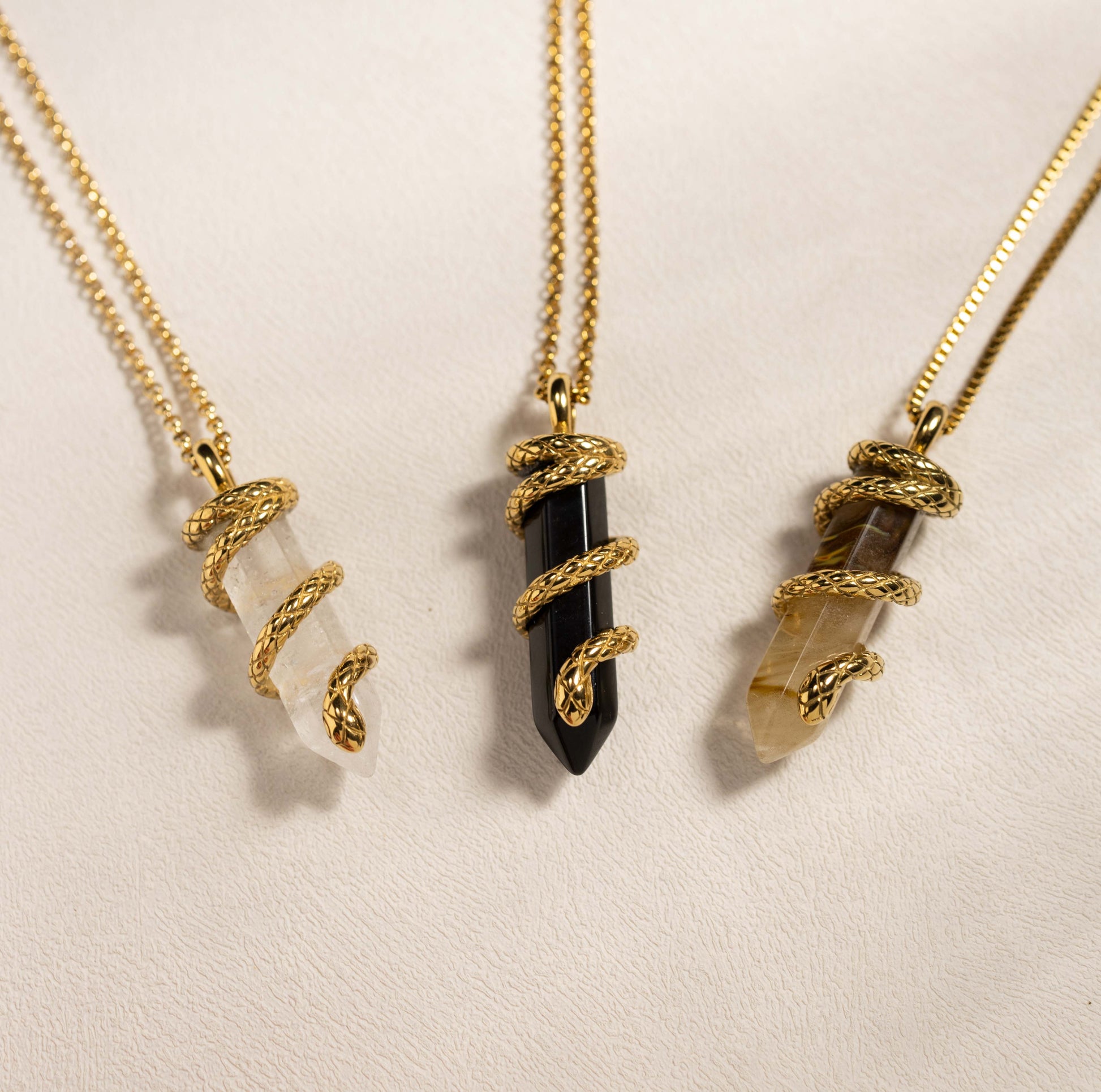 Silvbreeze Ouroboros serpent gemstone necklaces featuring obsidian, clear quartz, and tiger eye displayed together