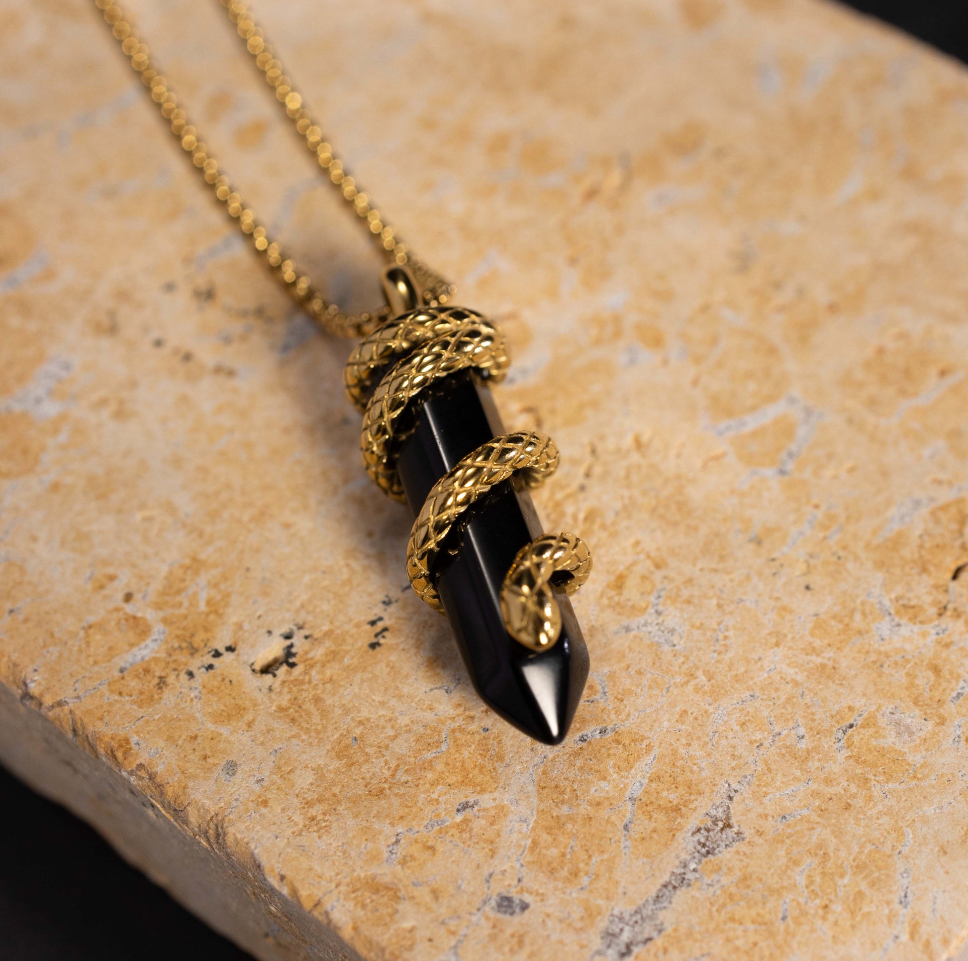 Silvbreeze Ouroboros serpent obsidian necklace in a close-up lifestyle scene, highlighting the black gemstone and gold serpent coil