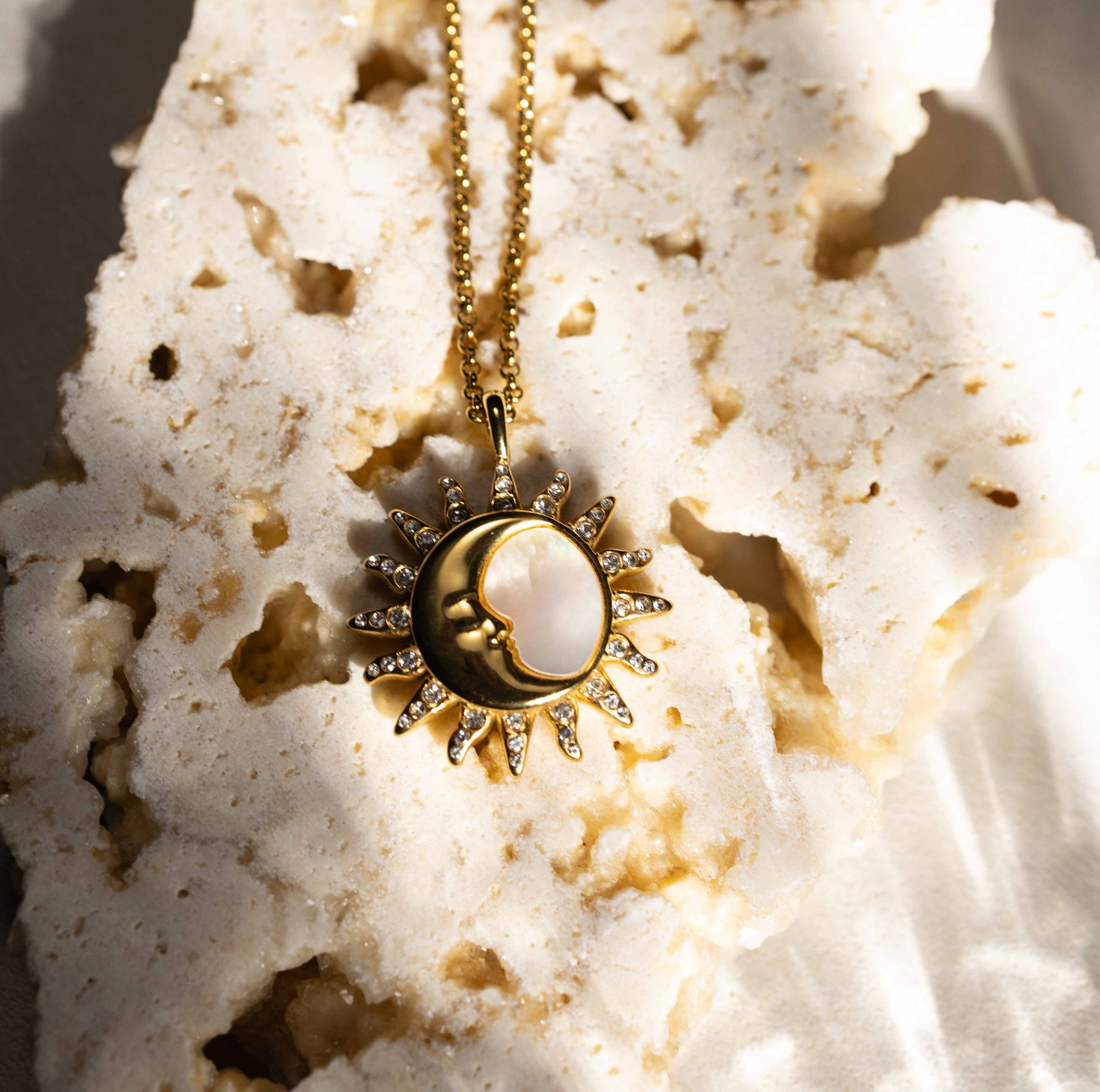 Detailed shot of the Silvbreeze "Selene Sol" gold pendant resting on a rugged stone, capturing the divine union of the sun and moon deities in sunlight.