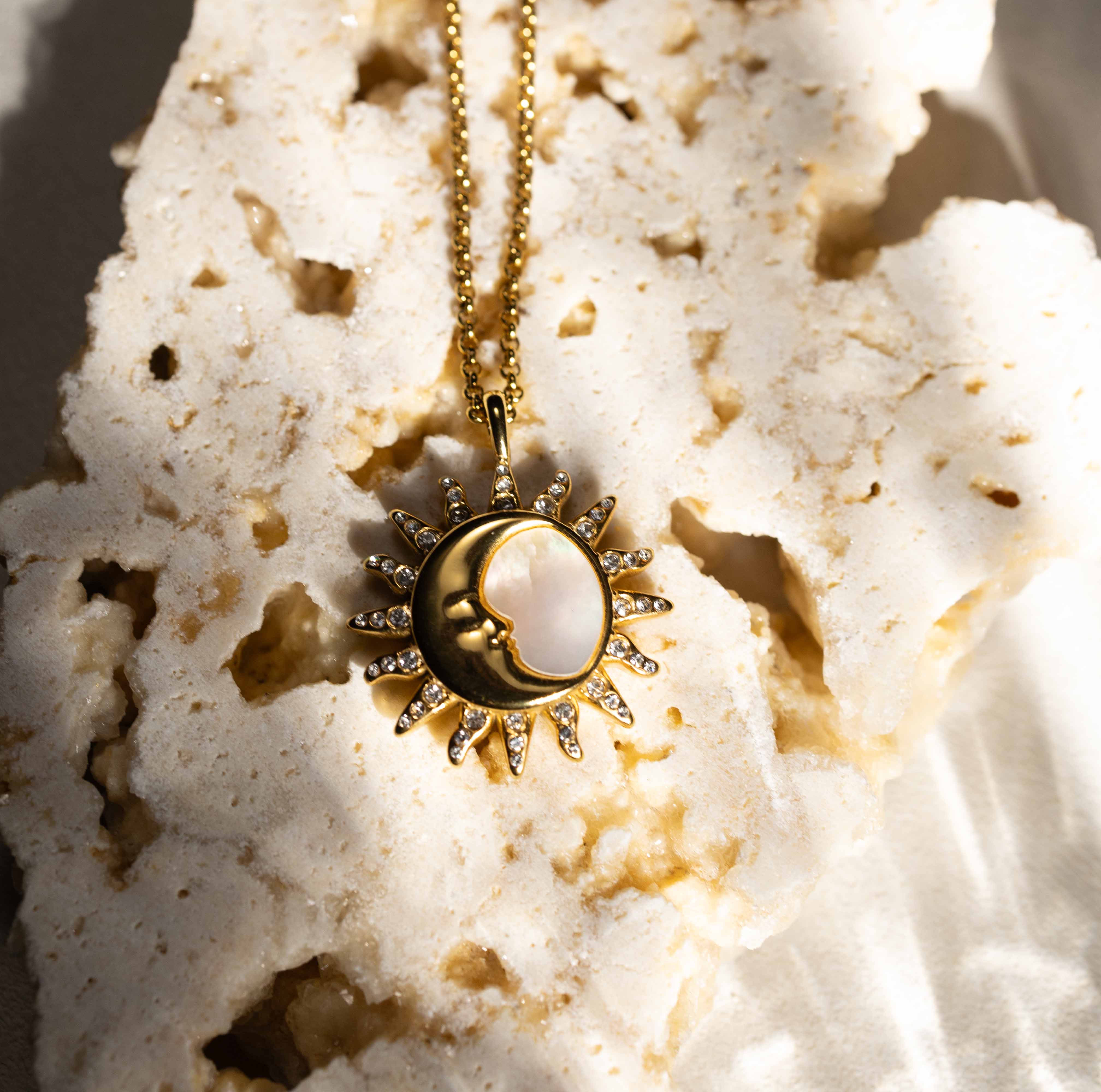 Detailed shot of the Silvbreeze "Selene Sol" gold pendant resting on a rugged stone, capturing the divine union of the sun and moon deities in sunlight.