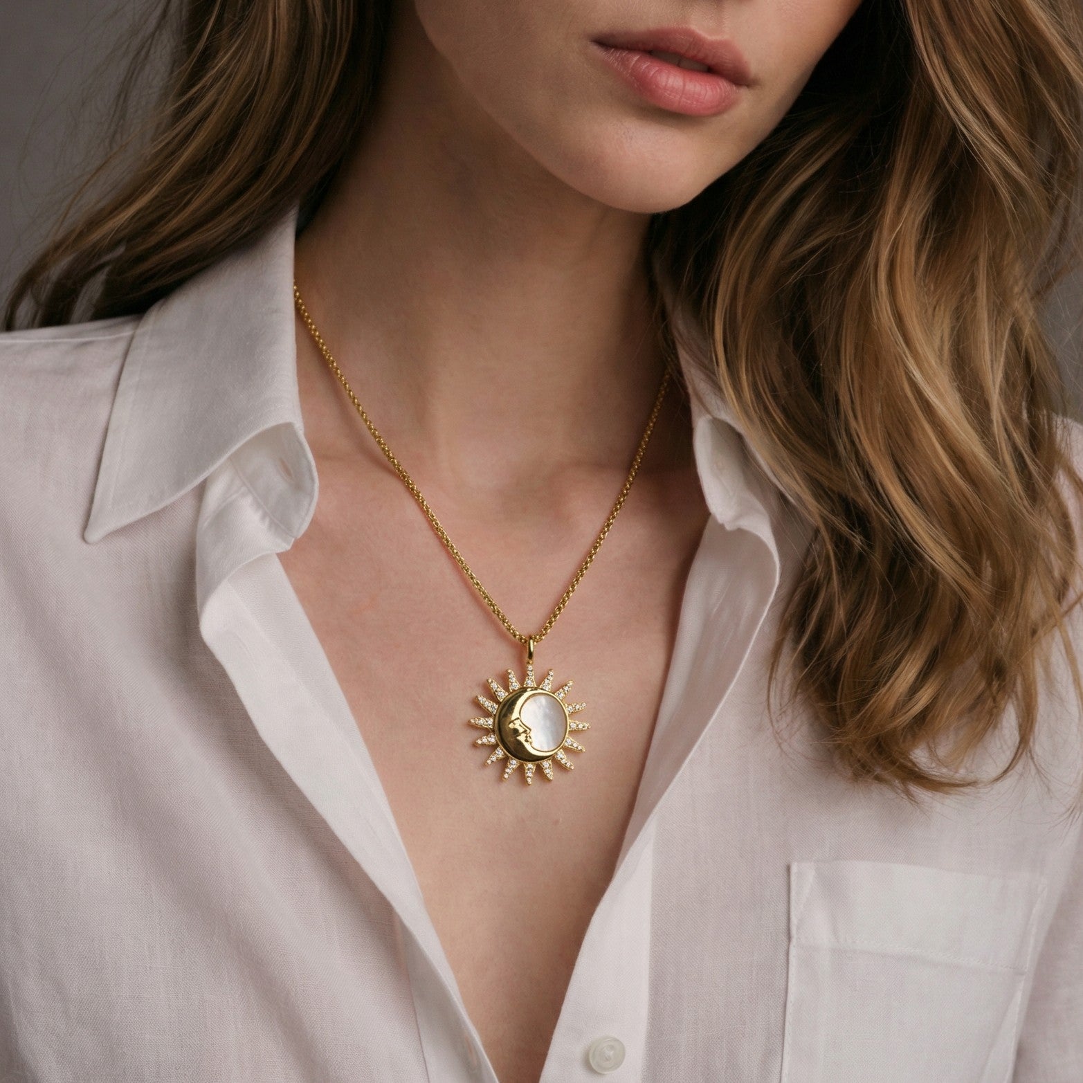 A lifestyle shot of a model wearing the Silvbreeze gold sun and crescent moon pendant necklace with a white shirt, showcasing the pendant size and the texture of the round box chain.