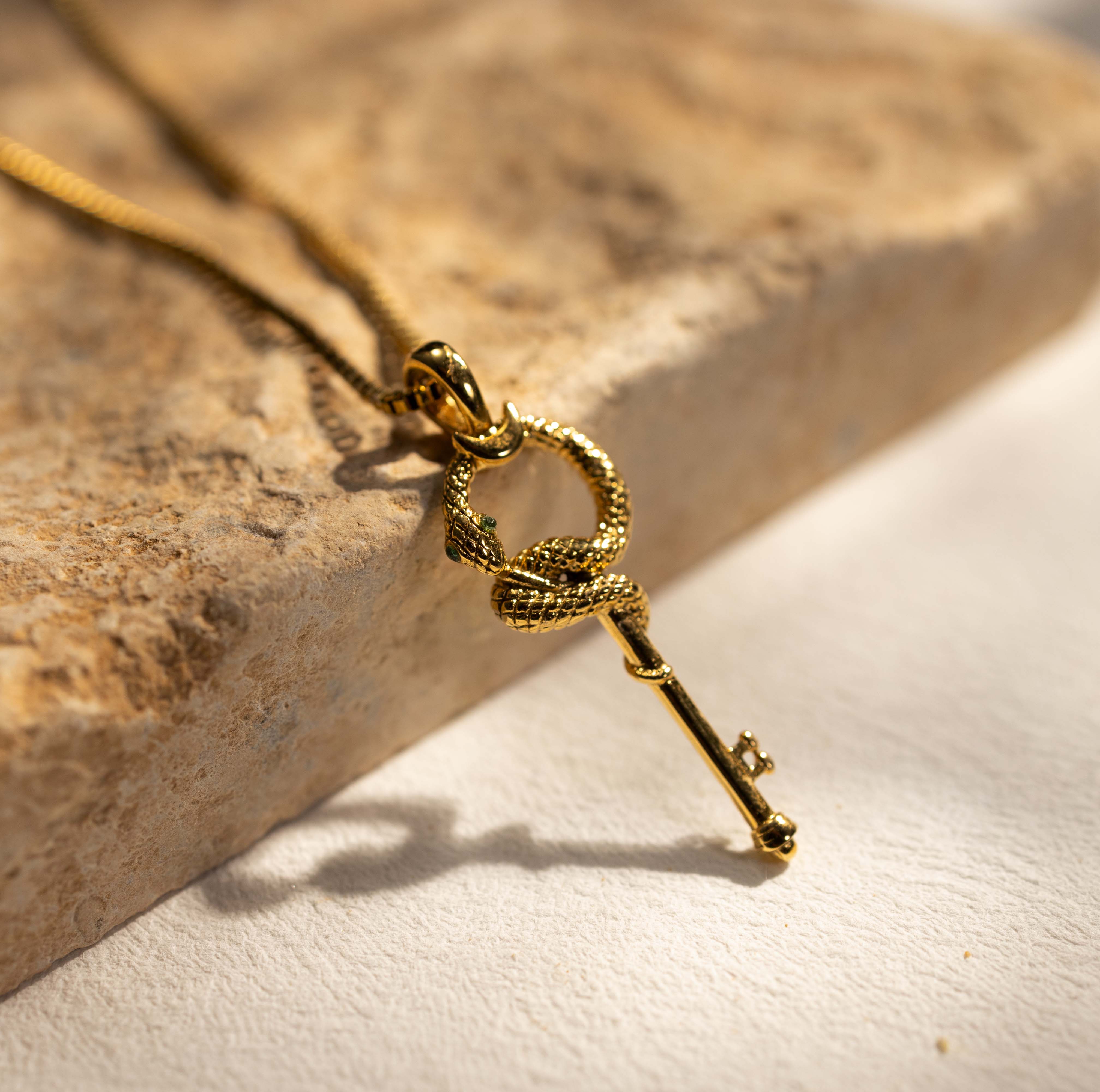 Close-up of Silvbreeze gold serpent key necklace resting on stone, emphasizing the flowing serpent form and key silhouette