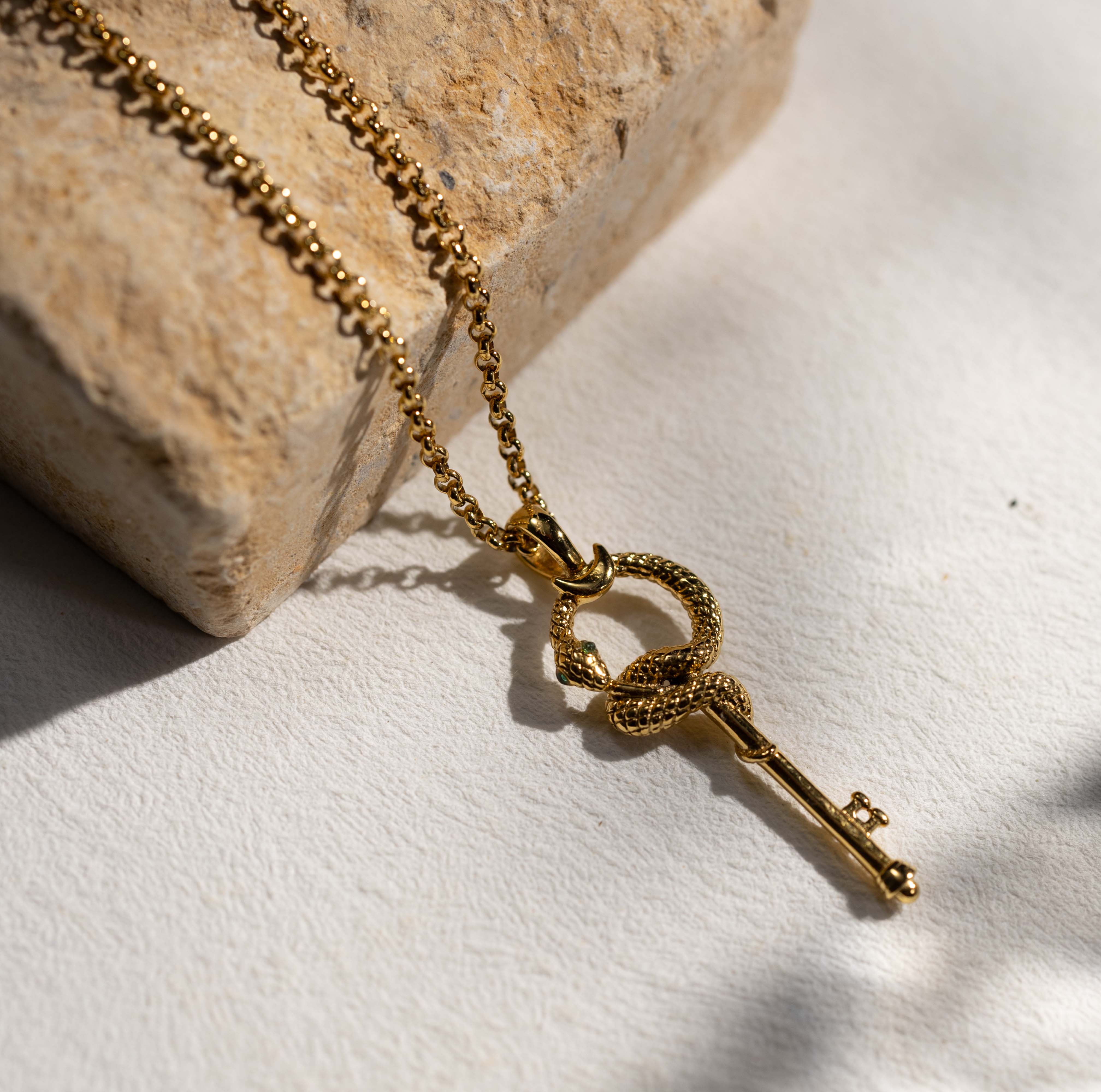 Silvbreeze gold serpent key necklace featuring a rolo chain, styled on natural stone to highlight the coiled snake and key pendant design