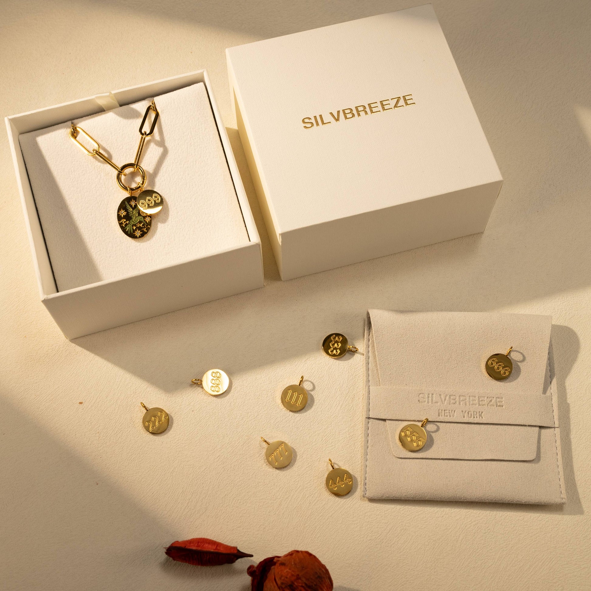 Silvbreeze paperclip O-clasp necklace with bluebird and angel number 999 charms displayed with gift boxes and packaging in a styled flatlay.